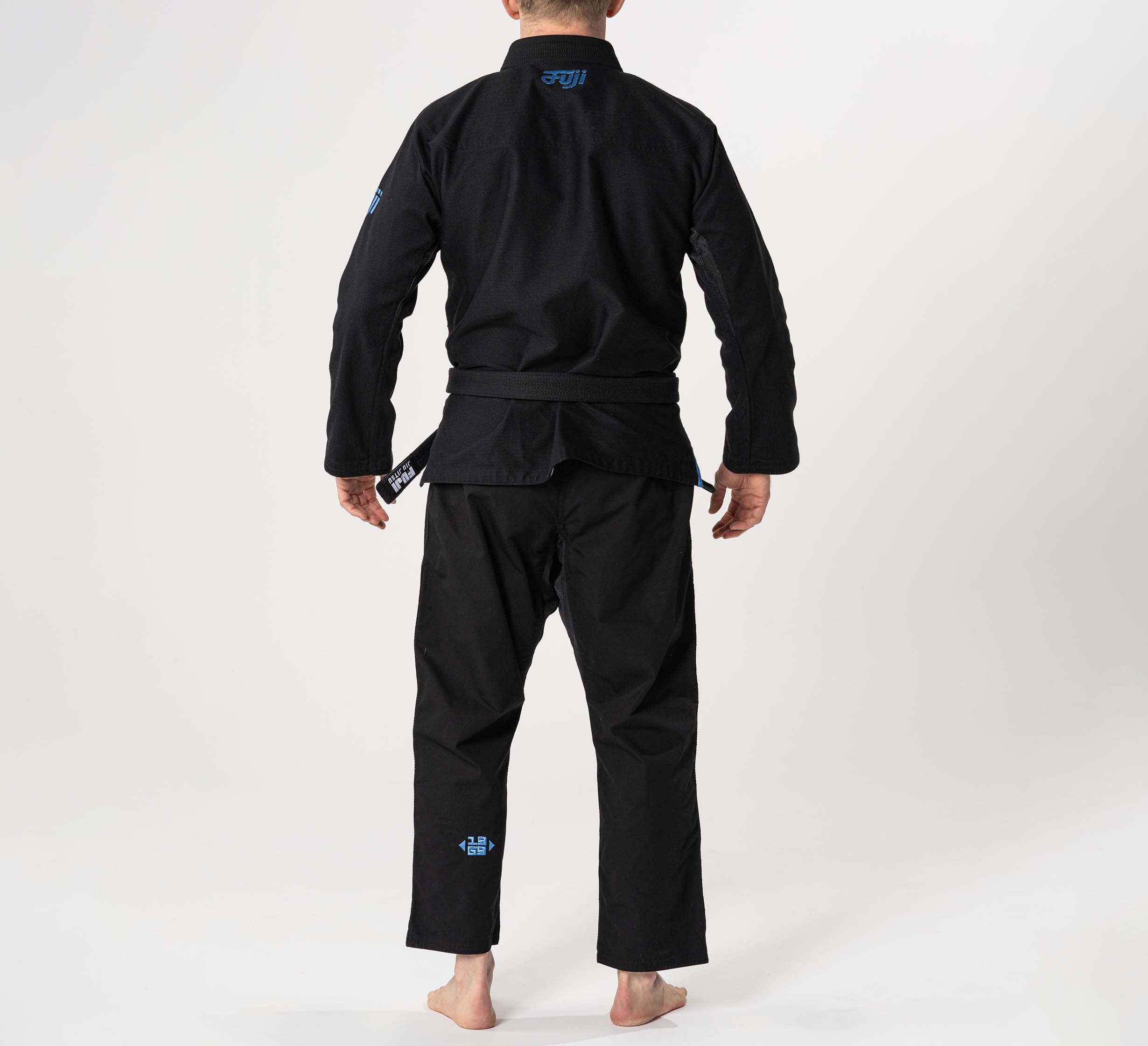 A person stands barefoot on a white background, shown from the back, wearing the Flow-Tech BJJ Gi Black/Blue/Grey martial arts uniform with a belt.