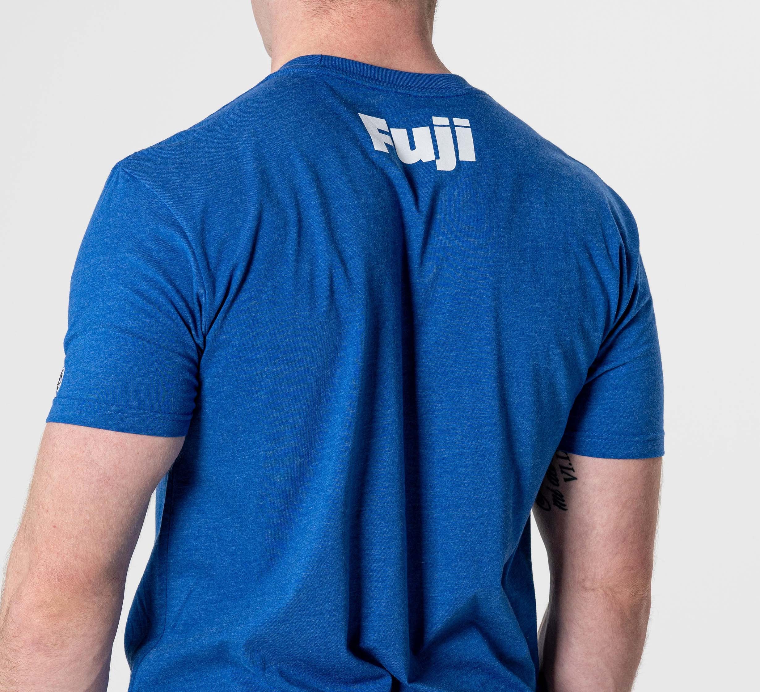 A person wearing the Jiu Jitsu Player T-Shirt Blue, featuring "Fuji" printed in white on the upper back, stands against a plain light background.
