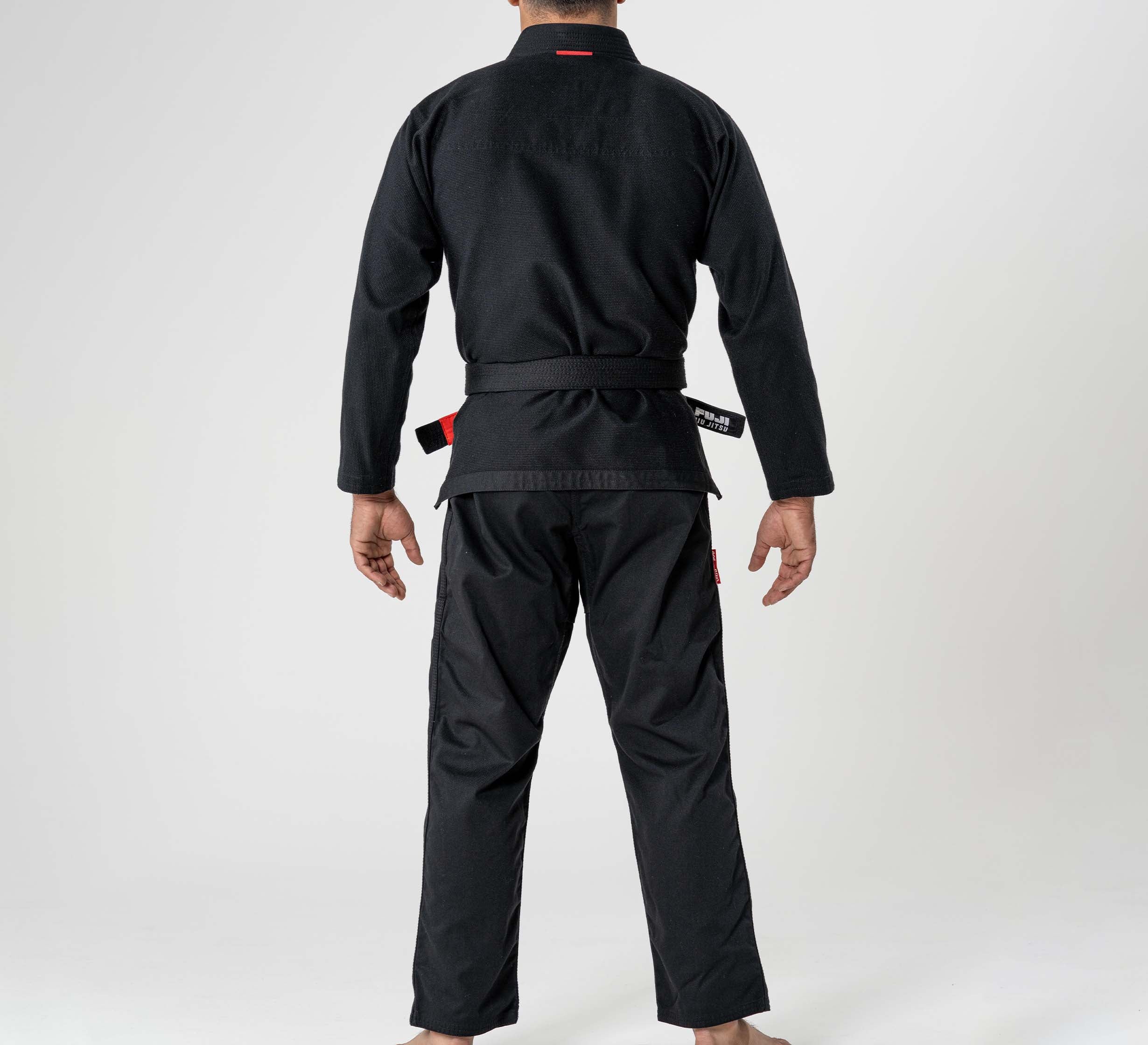 A person wears the Ultra Lite 300 BJJ Gi Black and a black belt, standing barefoot and facing away from the camera against a plain white background.