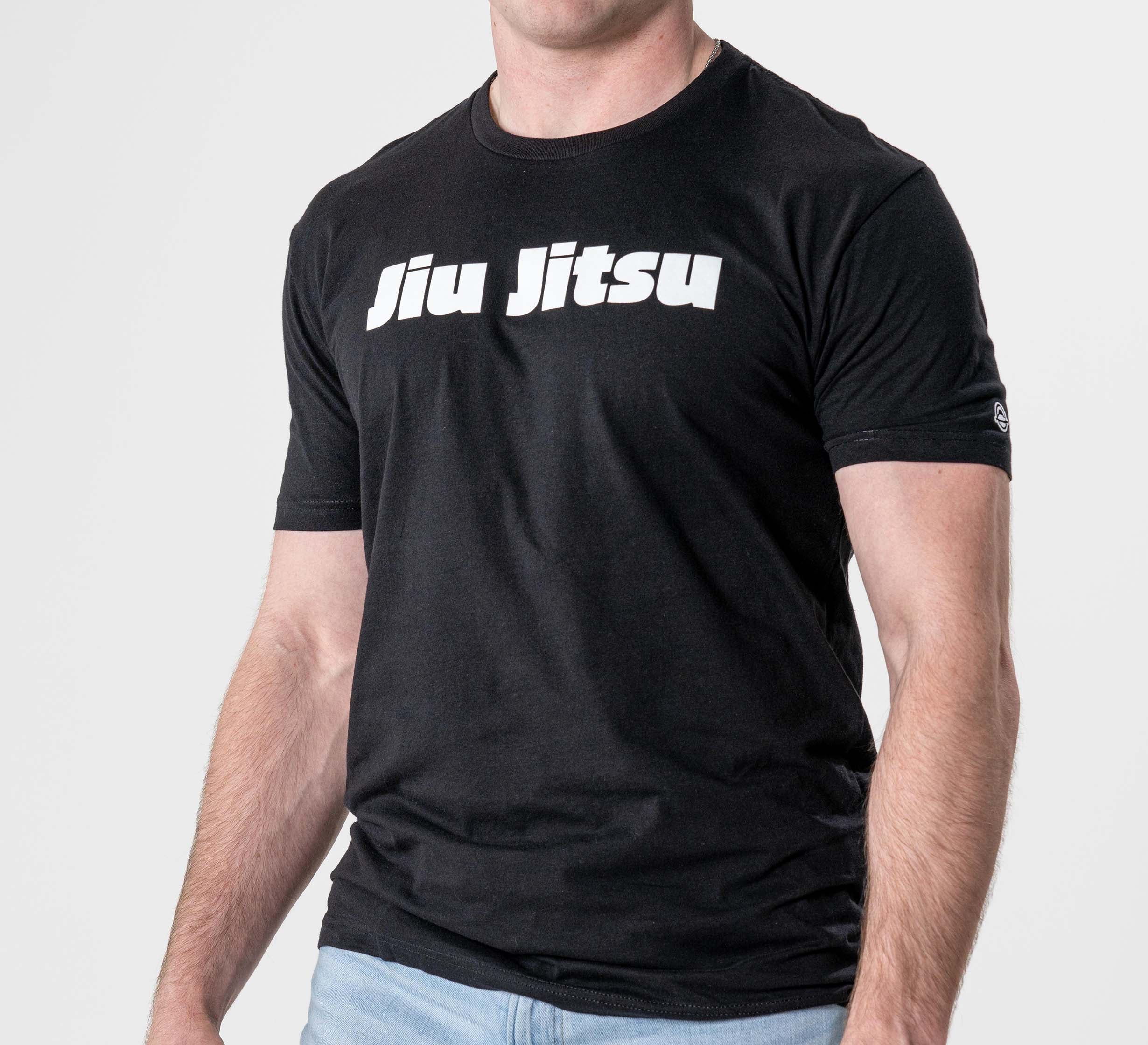 A person wearing the Jiu Jitsu Player T-Shirt Black, featuring bold white "Jiu Jitsu" text across the chest, paired with light blue jeans and standing against a plain white background.
