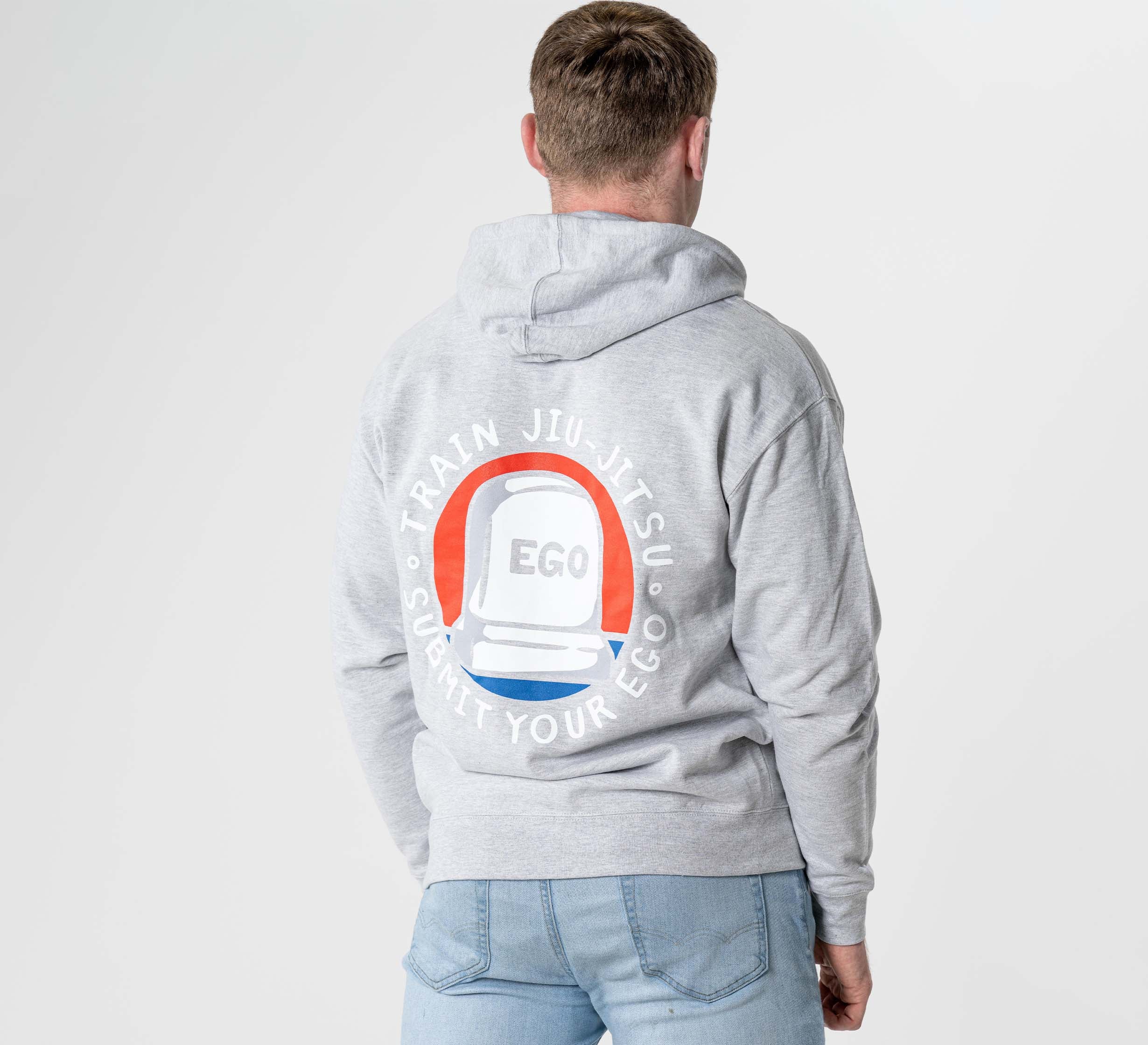A person wears the Submit Your Ego Hoodie in heather grey, featuring a white jiu-jitsu belt graphic and "EGO" with the circular text "Train Jiu-Jitsu Submit Your Ego" on the back.
