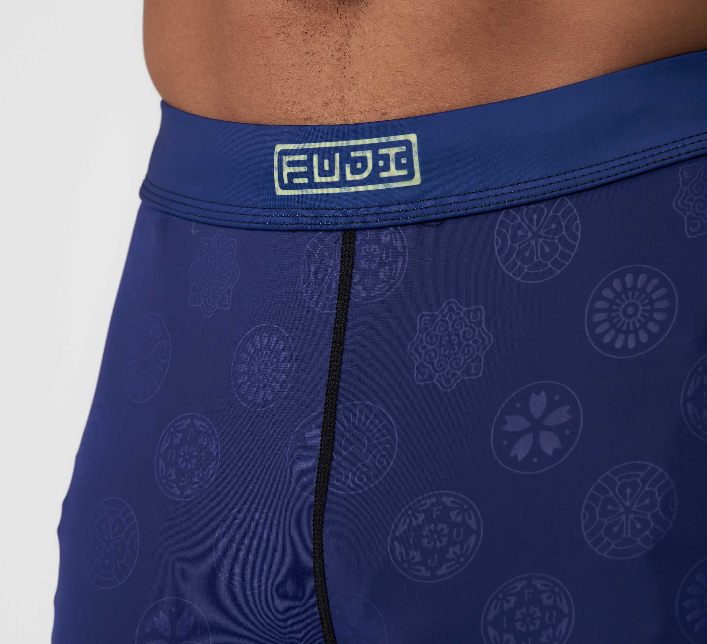 Close-up of a person wearing Shogun Heat Gear Spats Navy, featuring a FUDI logo on the waistband and geometric circular designs.