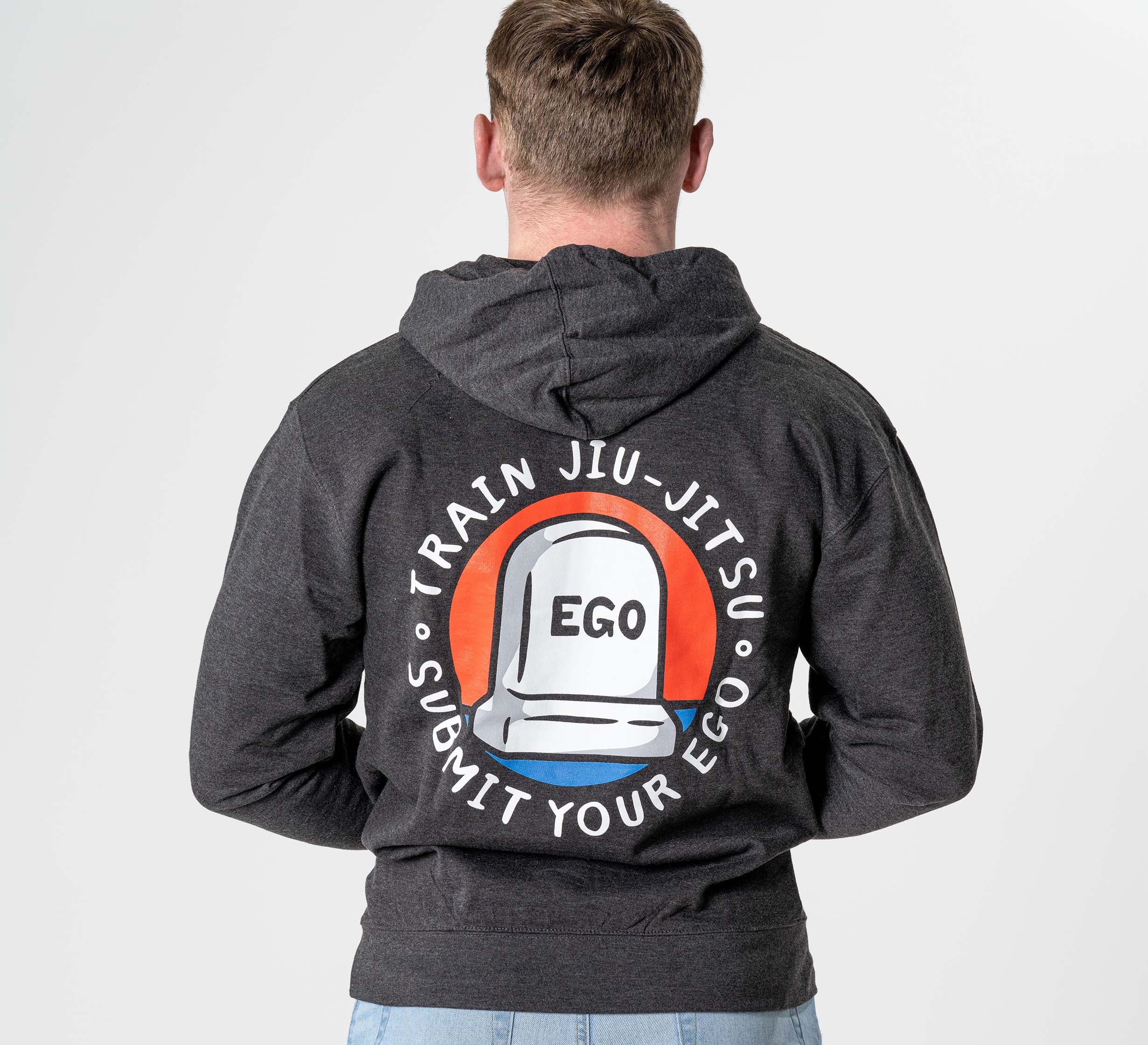 Seen from behind, a person wears the heather black Submit Your Ego Hoodie, featuring a tombstone graphic labeled "EGO" and the words "TRAIN JIU-JITSU SUBMIT YOUR EGO" in a circular design around it.