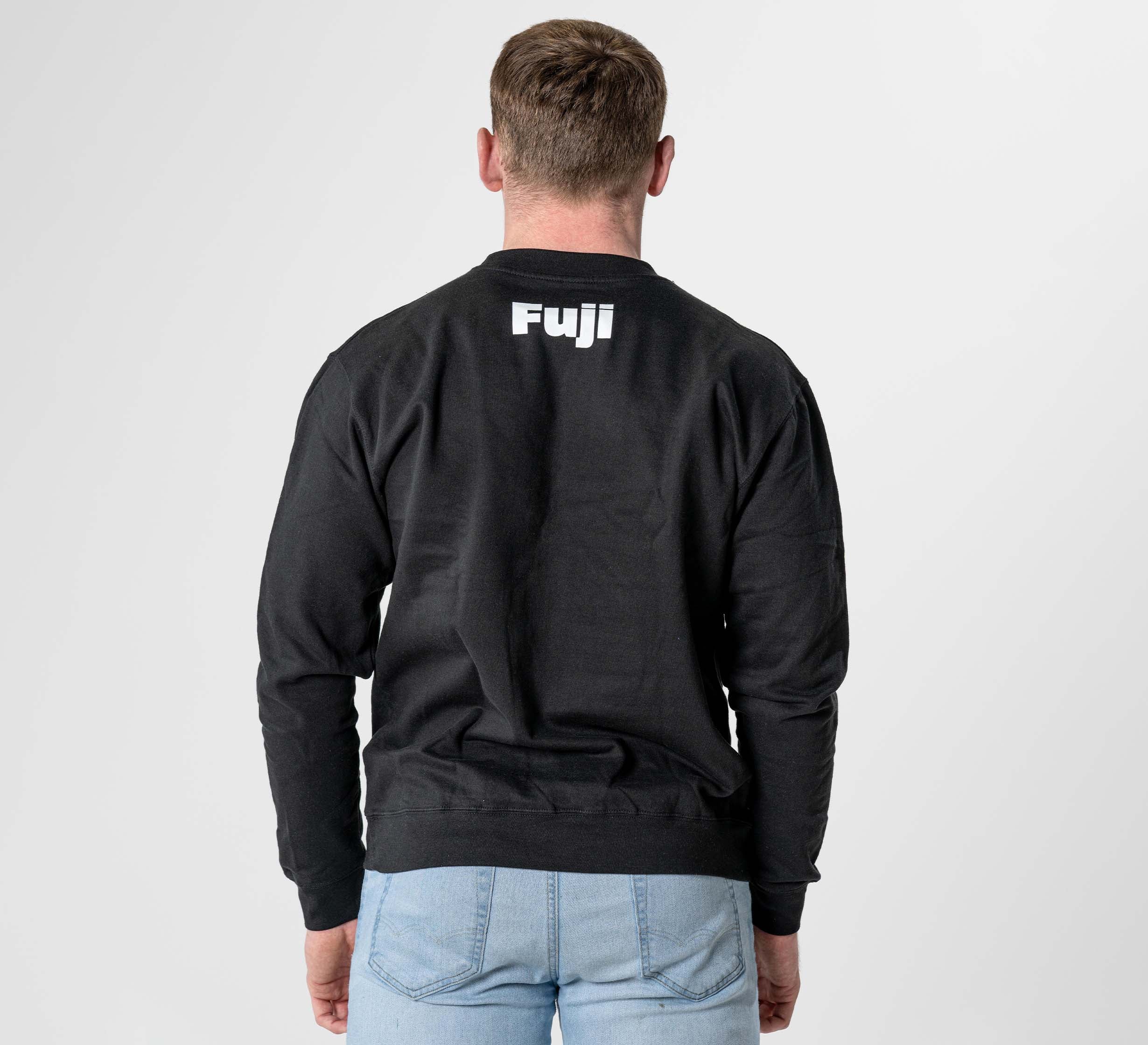 A person wearing the Jiu Jitsu Player Crewneck Black, featuring "Fuji" in white on the upper back, stands facing away against a light background. They are also dressed in light blue jeans.