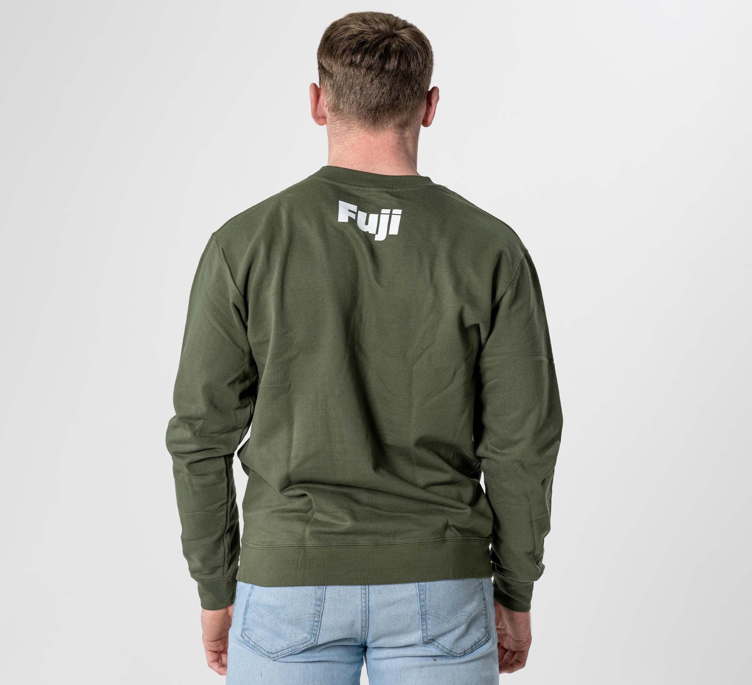 A person wearing the Jiu Jitsu Player Crewneck in military green with white "Fuji" print on the upper back, paired with light blue jeans and standing against a plain light background.