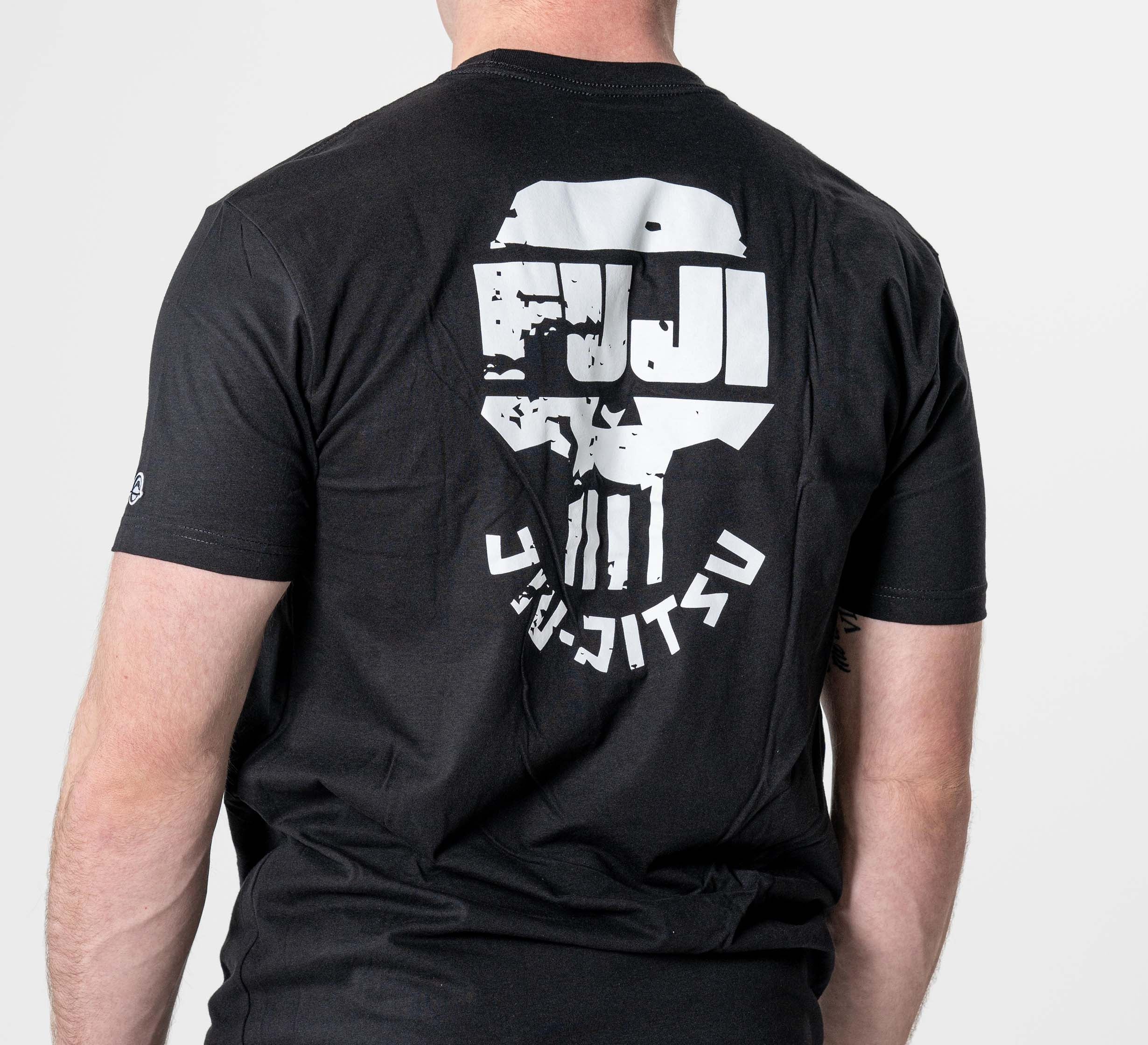 A man stands against a plain light background wearing the Punishment T-Shirt Black, featuring a white skull-like logo and “FUJI JIU JITSU” text on the back.