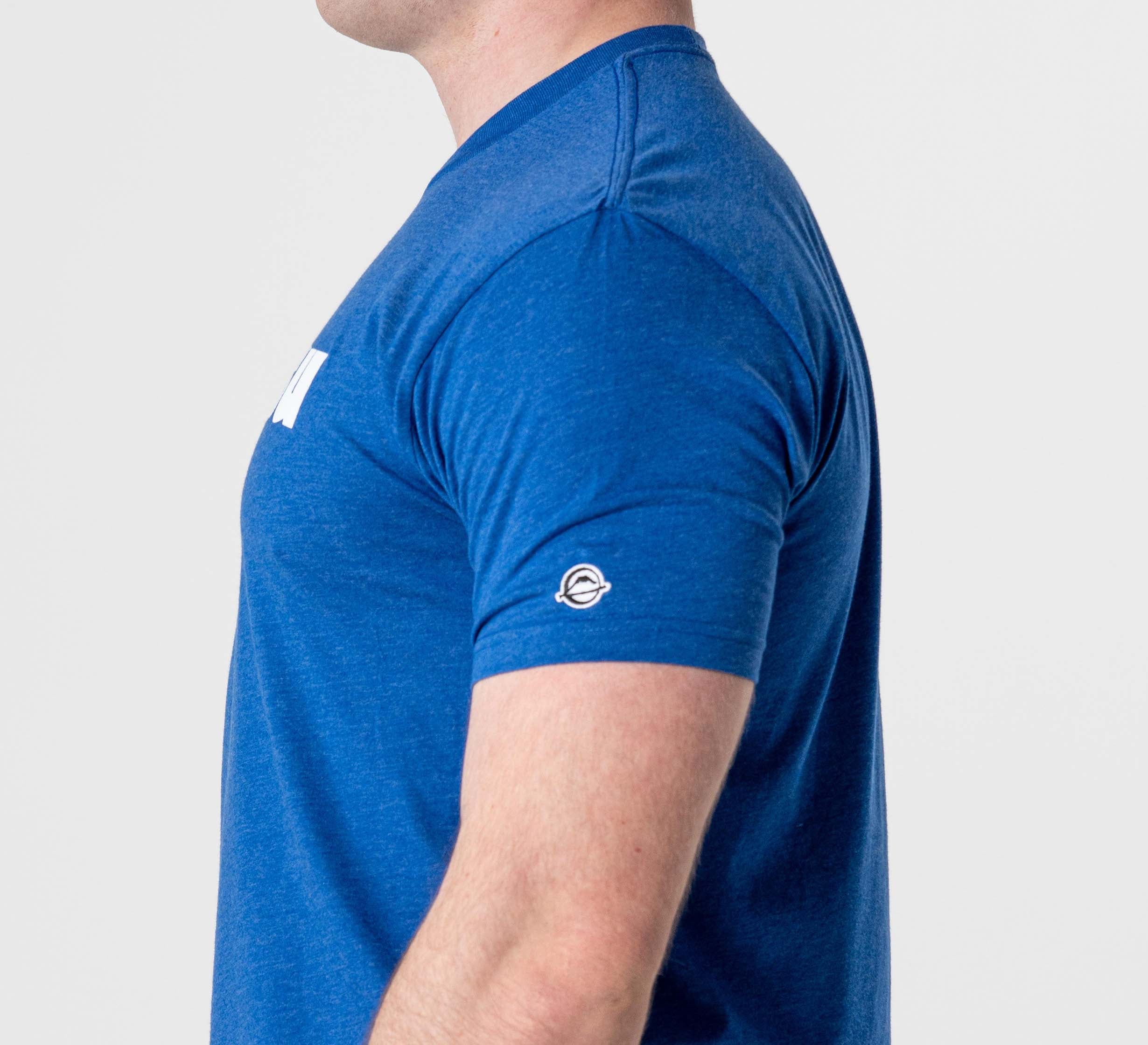 A person wearing the Jiu Jitsu Player T-Shirt Blue, featuring short sleeves and a small circular logo on the left sleeve, is shown from the side against a plain white background.