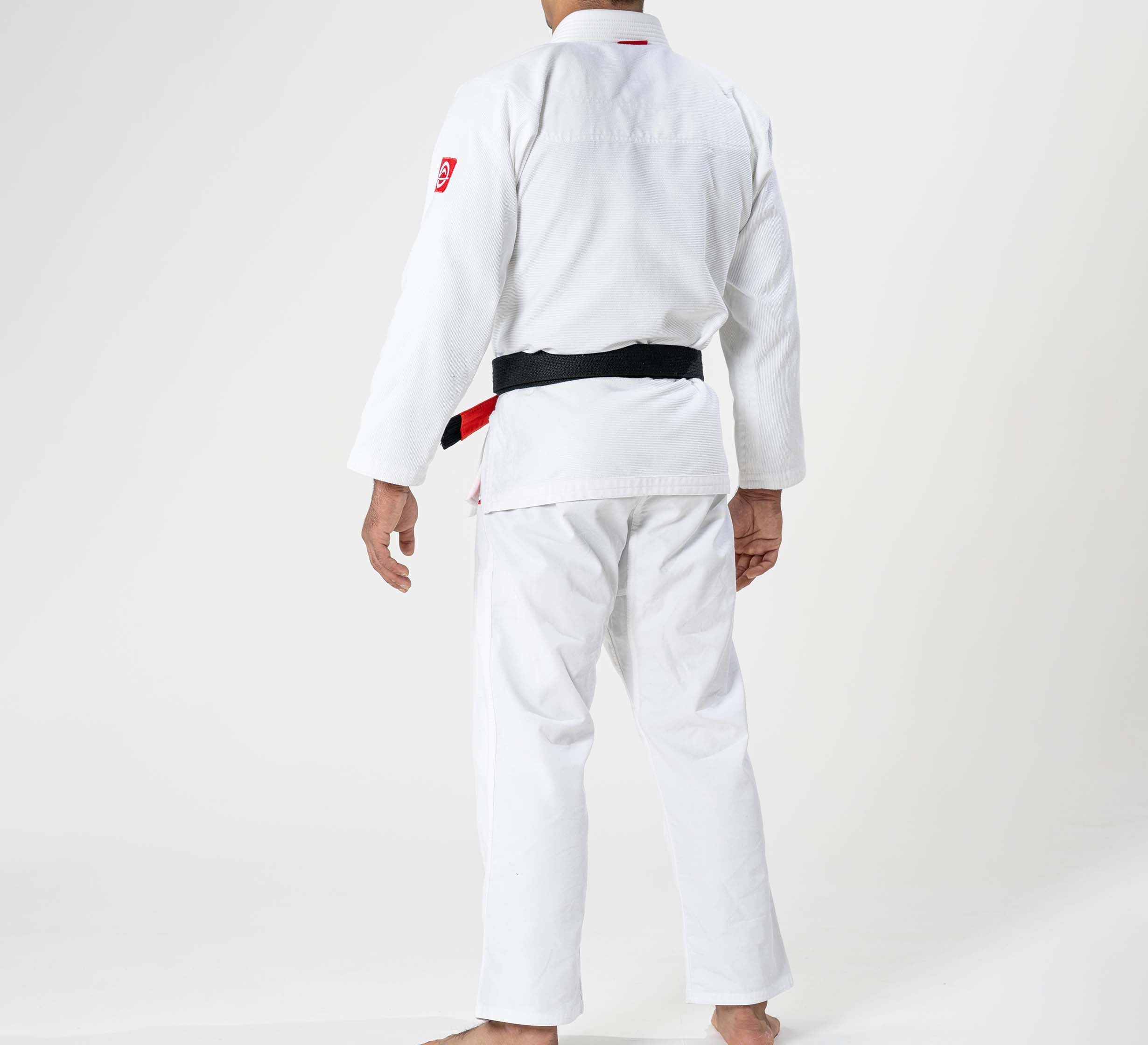 A child wearing the Kids Ultra Lite 300 BJJ Gi in white stands barefoot with their back to the camera against a plain white background.