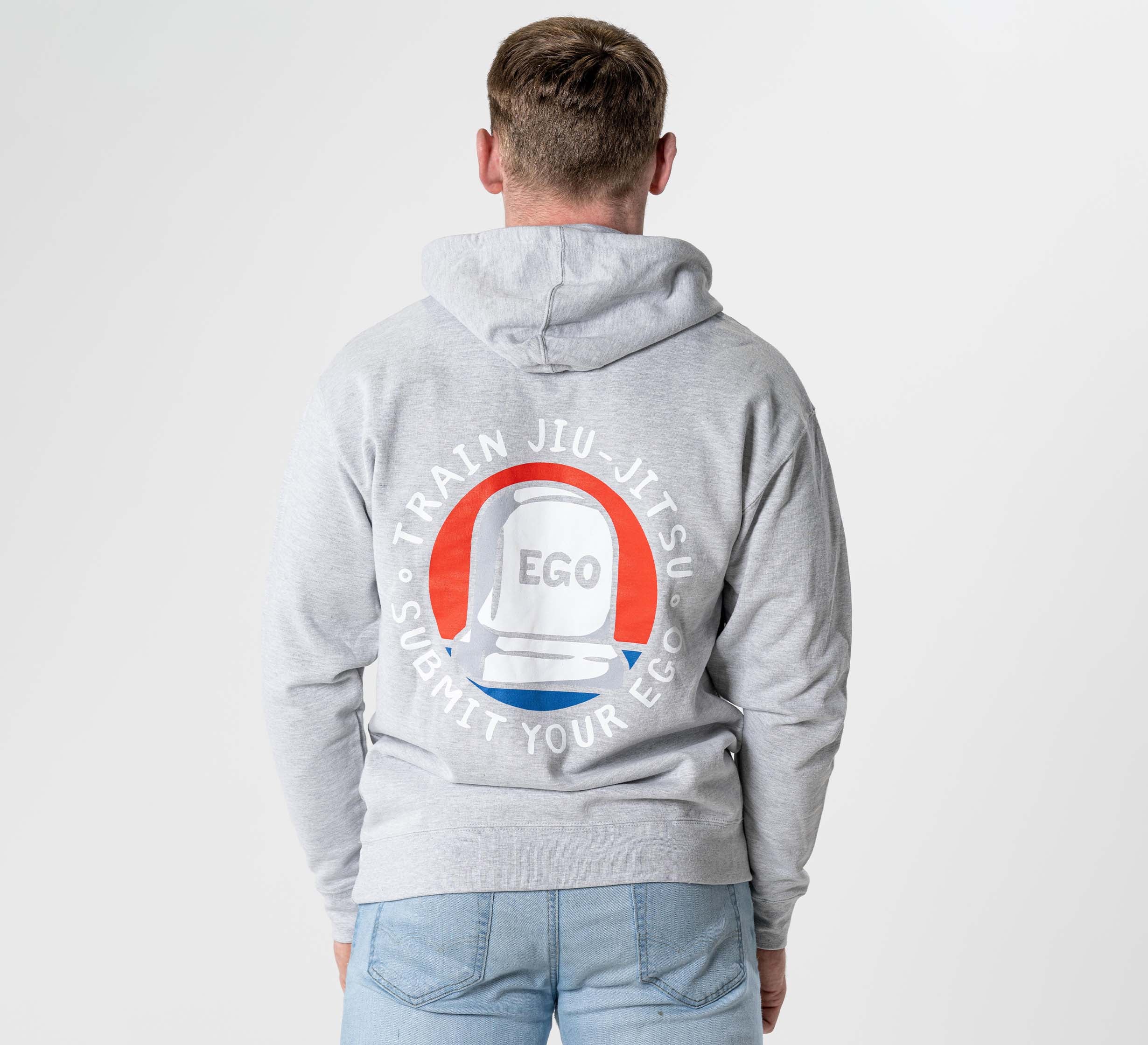 A person seen from the back wearing the Submit Your Ego Hoodie in heather grey, featuring a tombstone graphic labeled "EGO" and a circular "Train Jiu-Jitsu. Submit Your Ego" design with the hood down.