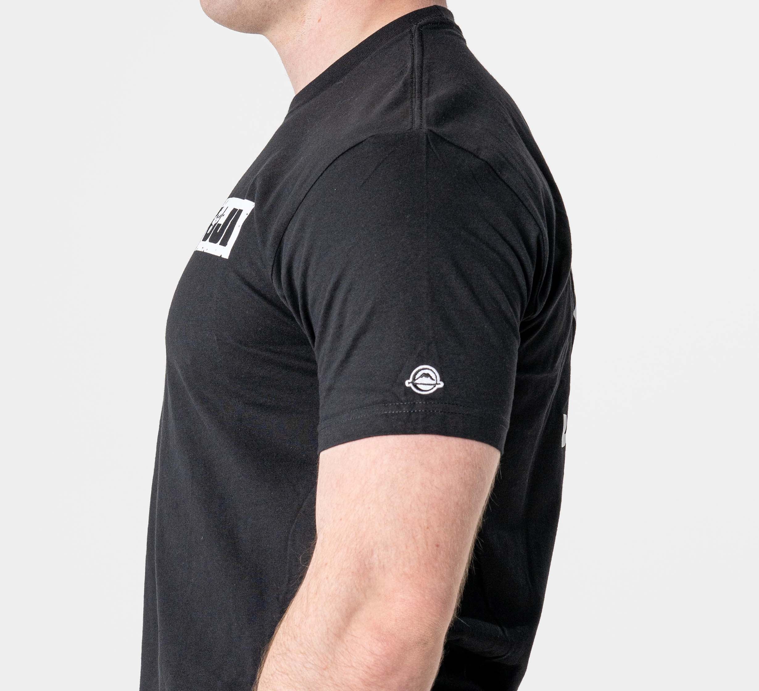 A person in profile wears the Punishment T-Shirt Black, featuring short sleeves, a small circular logo on the sleeve, and a rectangular white graphic on the chest, set against a plain white background.