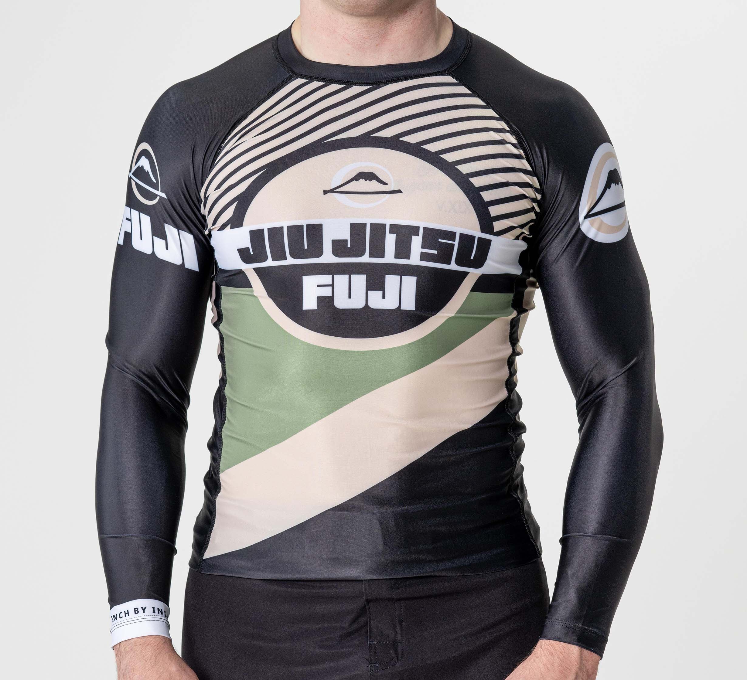 A person is wearing the Pacer Flex Lite Long Sleeve Rashguard Black, featuring beige and green accents, bold "JIU JITSU FUJI" text on the chest, and circular designs on the sleeves and front; their face is not visible.