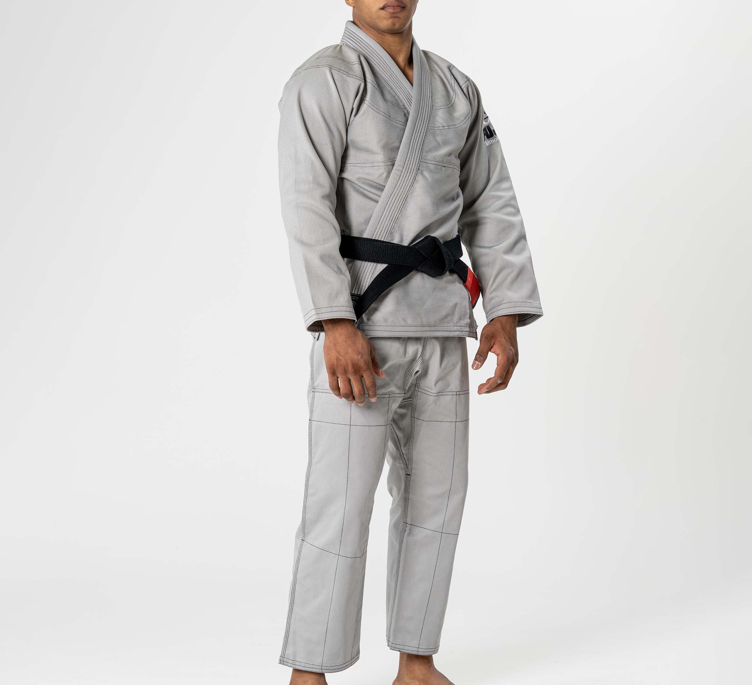 A person stands barefoot against a plain white background, wearing the Lightweight BJJ Gi Grey with a black belt. Their face is partially out of the frame.