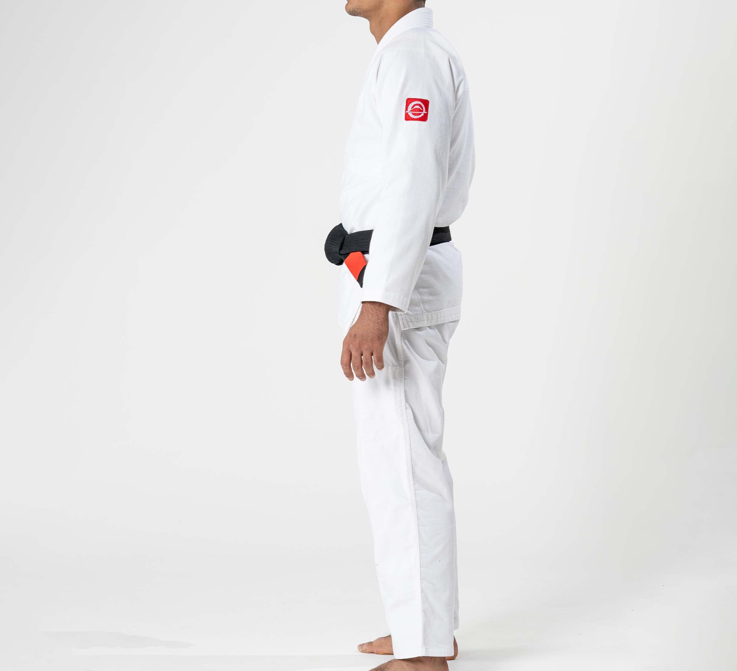 A barefoot person in profile wears the Ultra Lite 300 BJJ Gi White with a black belt and a red patch on the upper sleeve, standing against a plain white background.