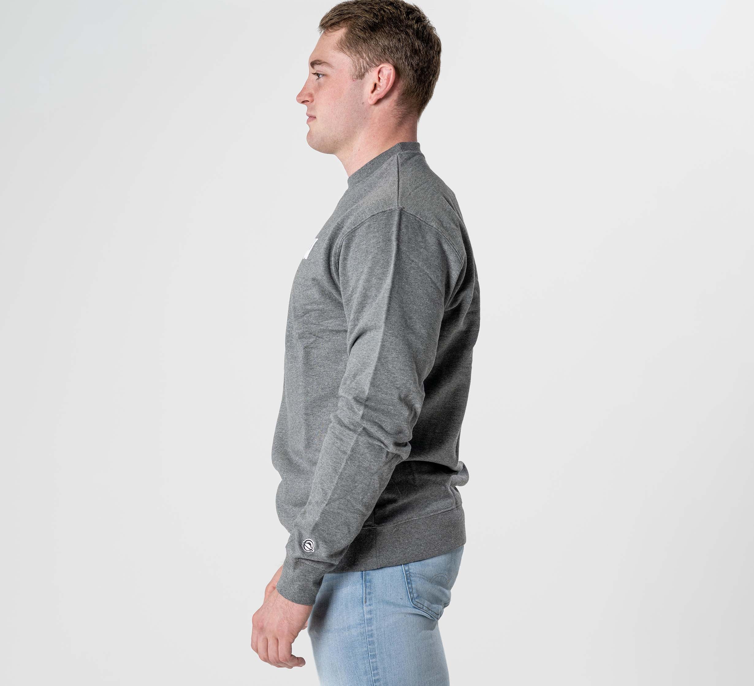 A man in profile facing left wears the Jiu Jitsu Player Crewneck Heather Grey with light blue jeans, set against a plain white background.