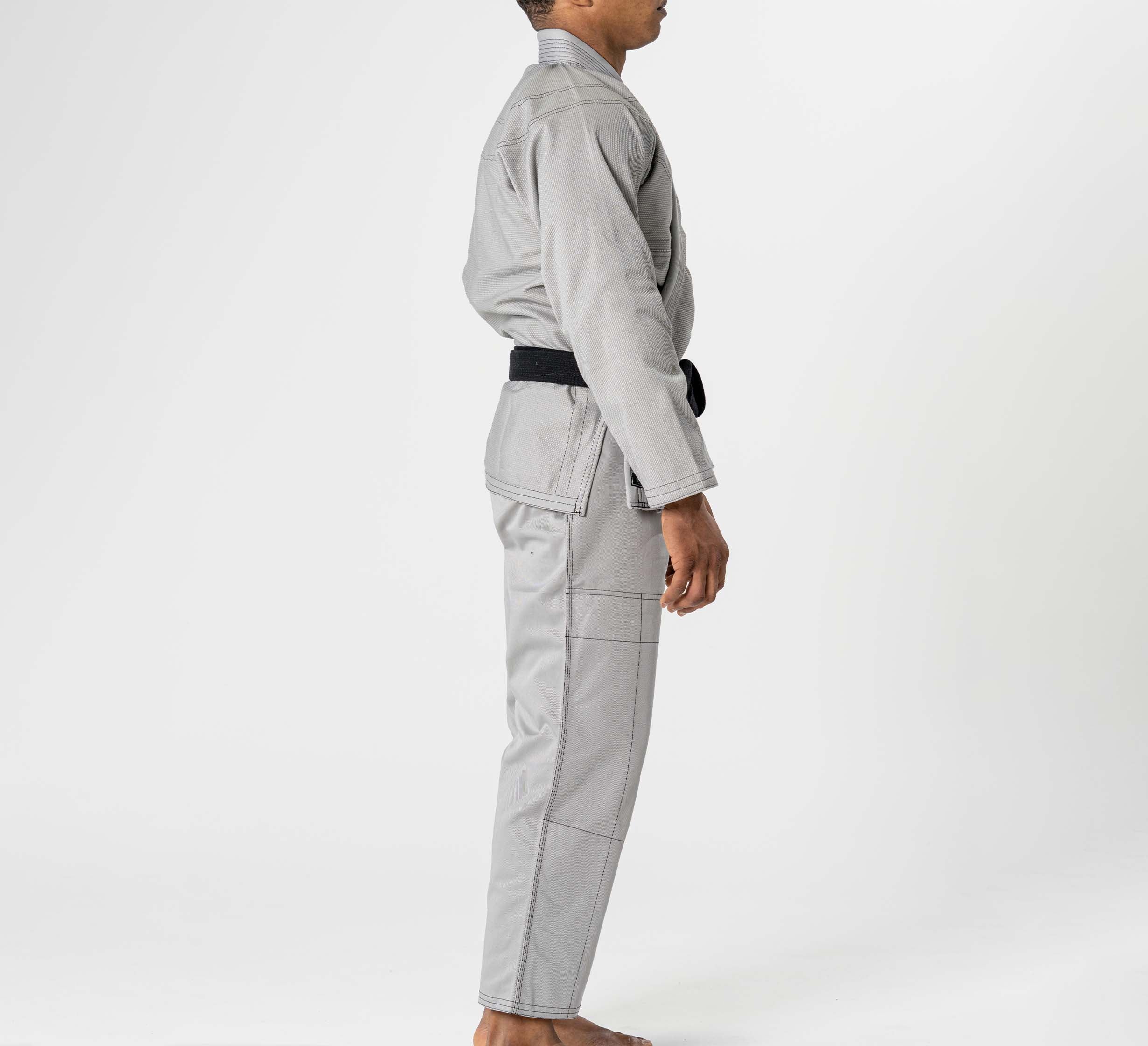 A person stands barefoot in profile, dressed in the Lightweight BJJ Gi Grey with a black belt, set against a plain white background.