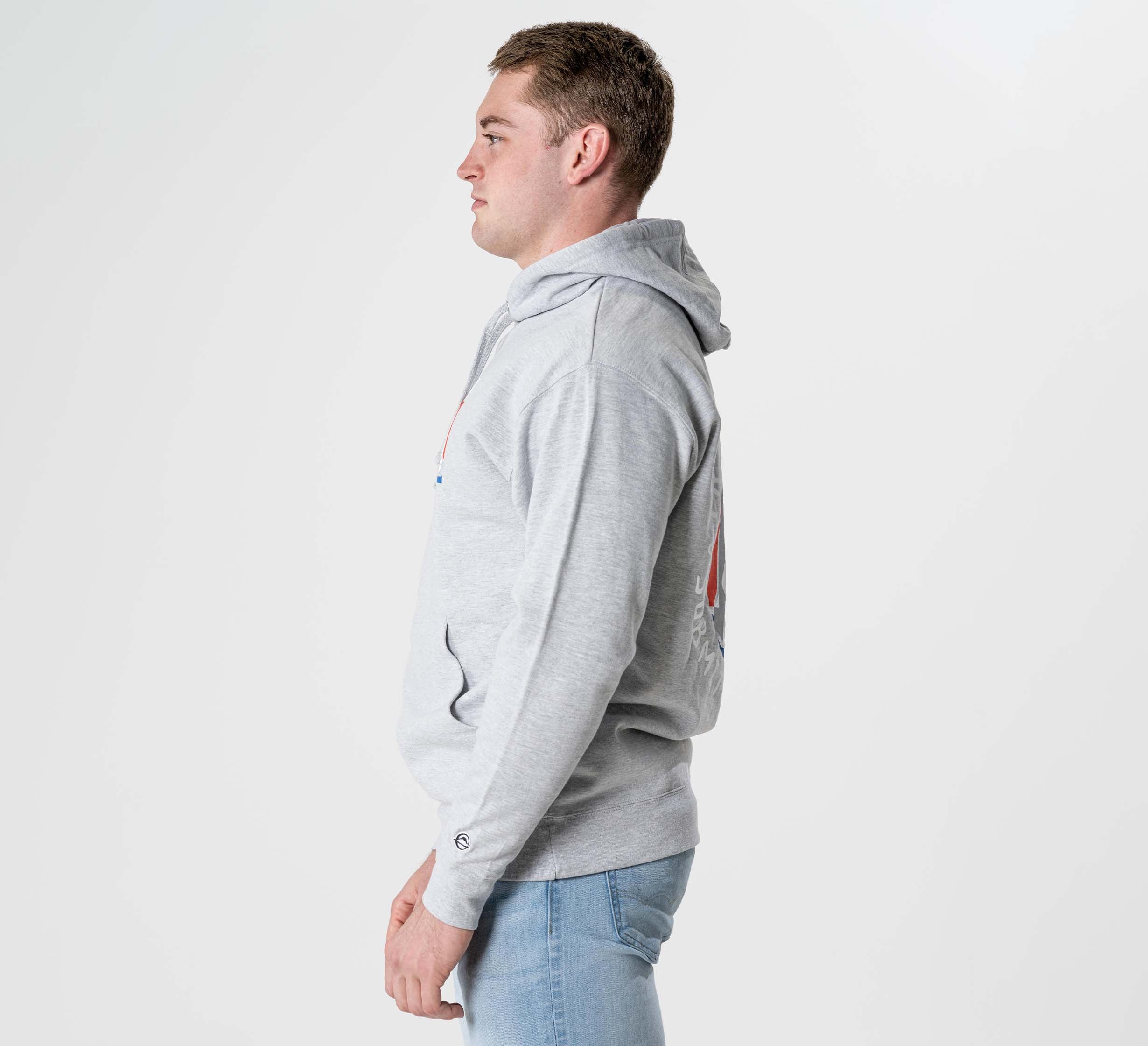 A man in a Submit Your Ego Hoodie Heather Grey and light blue jeans stands in profile against a plain white background.