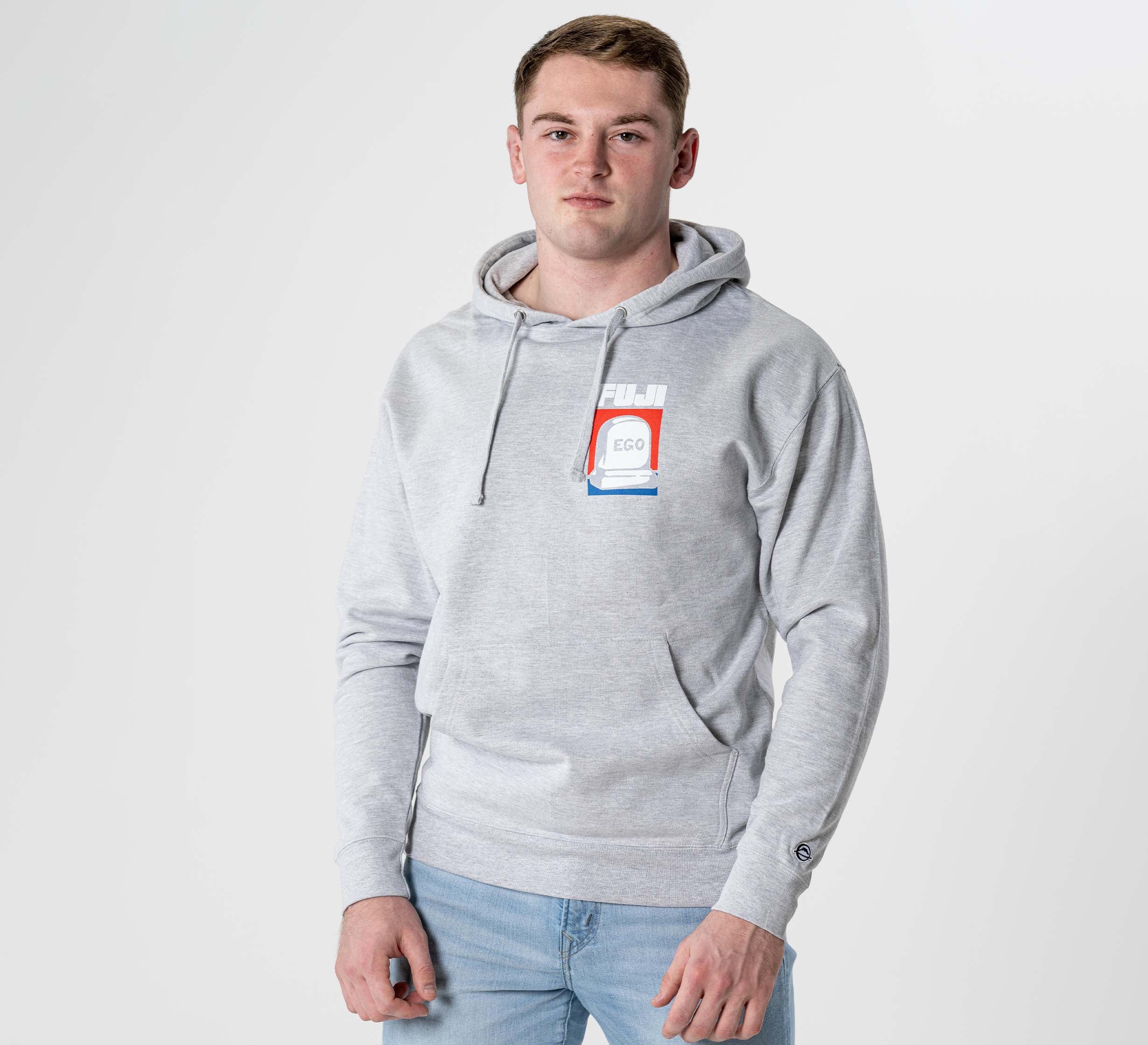 A young man with short light brown hair wears a Submit Your Ego Hoodie in Heather Grey and light blue jeans, standing against a plain white background.