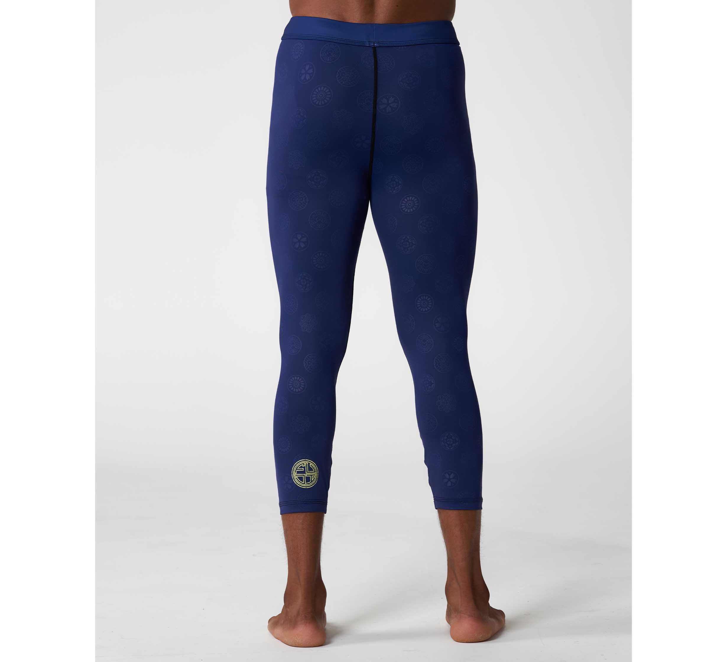 A person stands barefoot, facing away, wearing Shogun Heat Gear Spats Navy—fitted athletic leggings with subtle patterns and a small circular logo near the left ankle—against a plain, light-colored background.