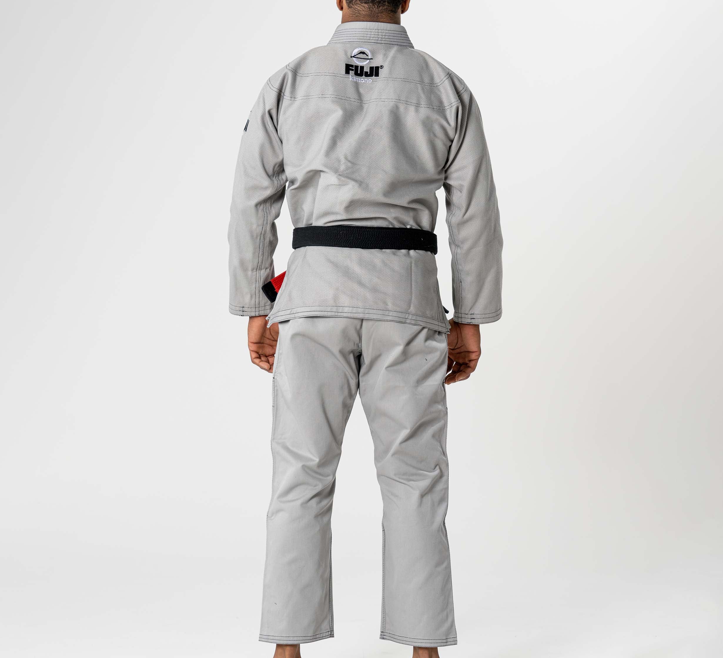 A person stands barefoot facing away, wearing the Lightweight BJJ Gi Grey with a black belt. "FUJI" is printed on the upper back. The background is plain white.