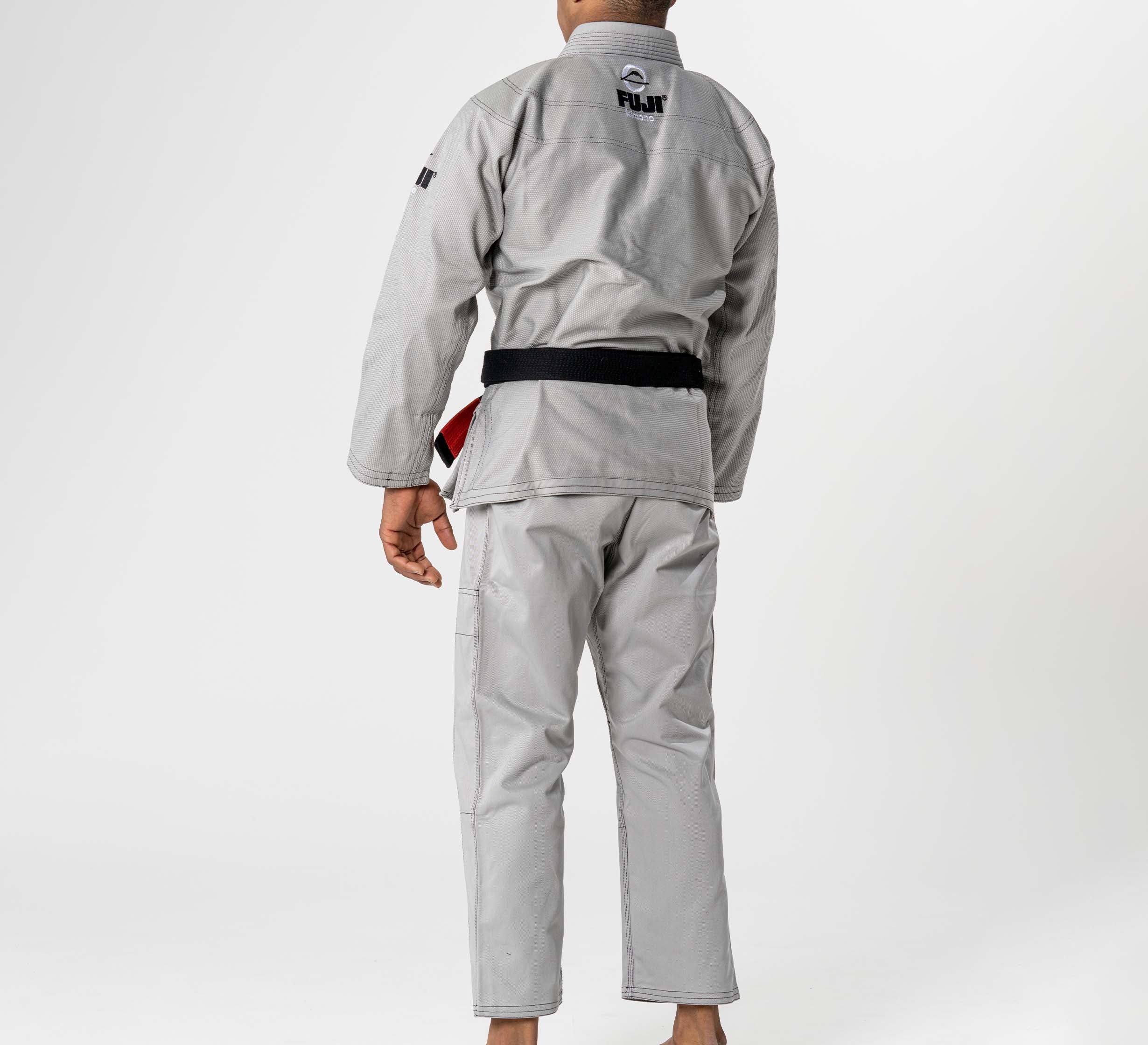 A barefoot person stands facing away in a Lightweight BJJ Gi Grey with a black belt. The gi features the Fuji logo on the upper back, set against a plain white background.