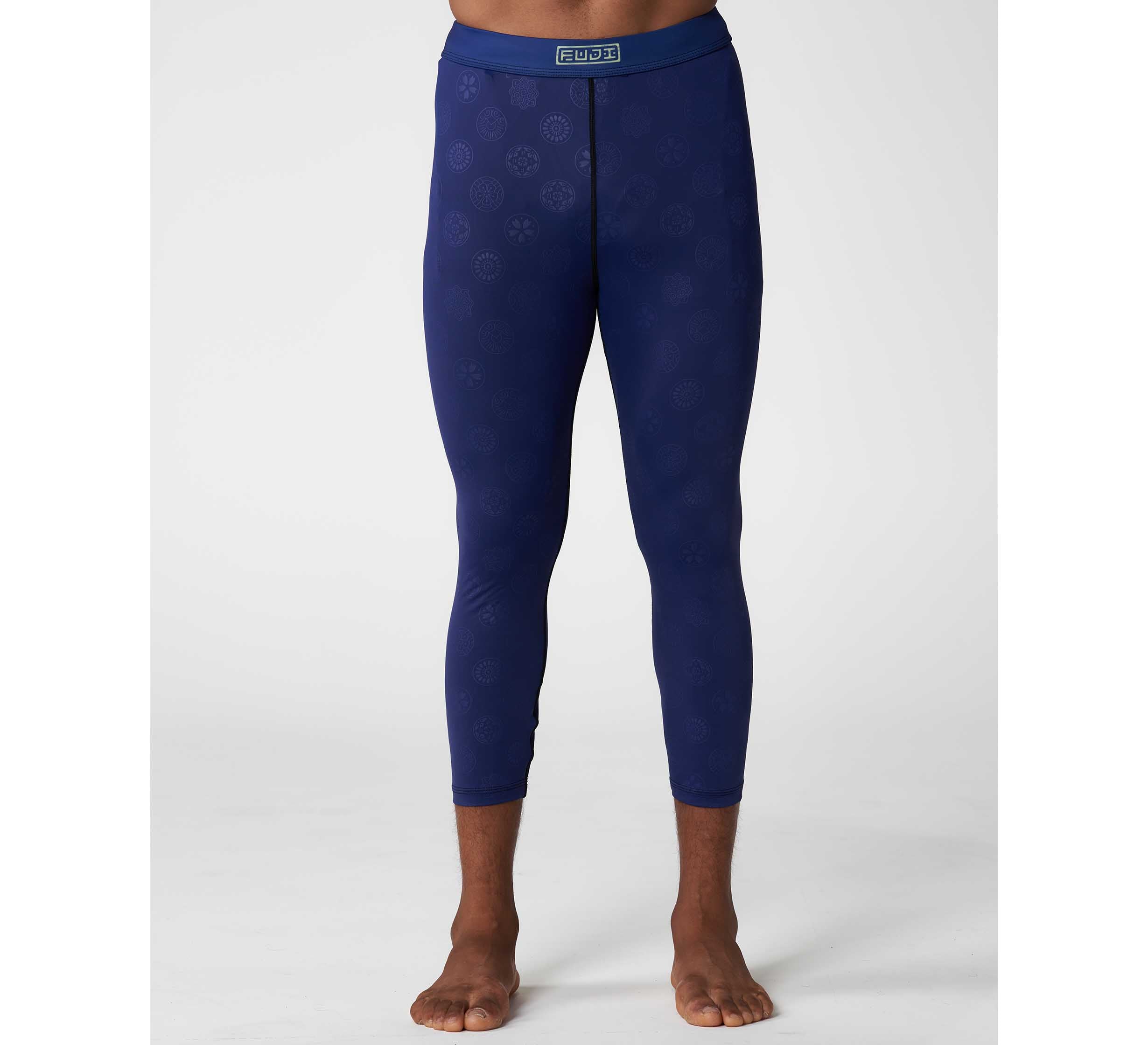 A person stands barefoot on a white background, showing only their legs and lower torso in fitted Shogun Heat Gear Spats Navy leggings with a subtle pattern and a FUDR-branded waistband.