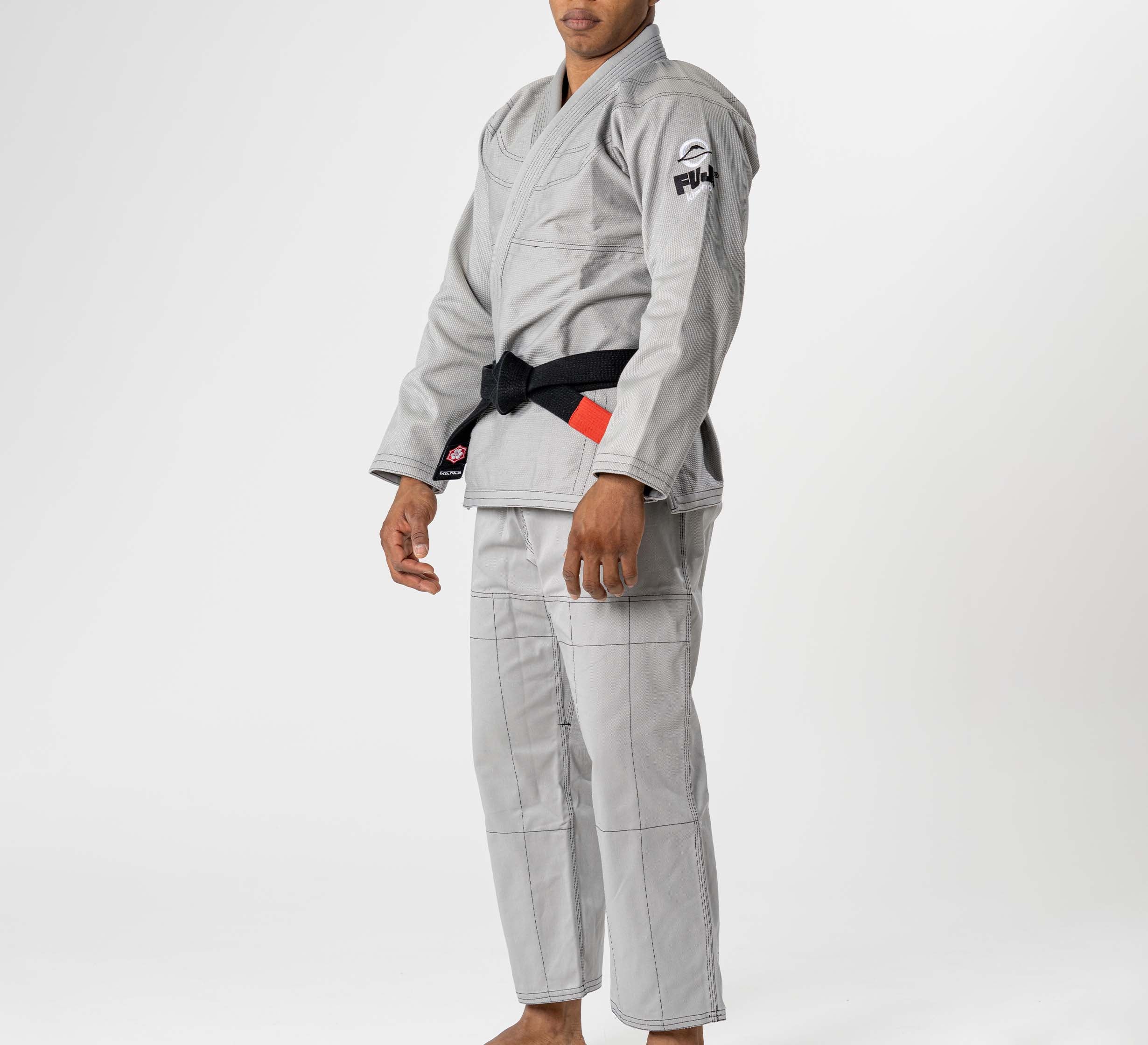 A person stands barefoot on a white background, facing forward with arms relaxed, wearing the Lightweight BJJ Gi Grey and black belt. The gi features FUJI branding on the sleeve.