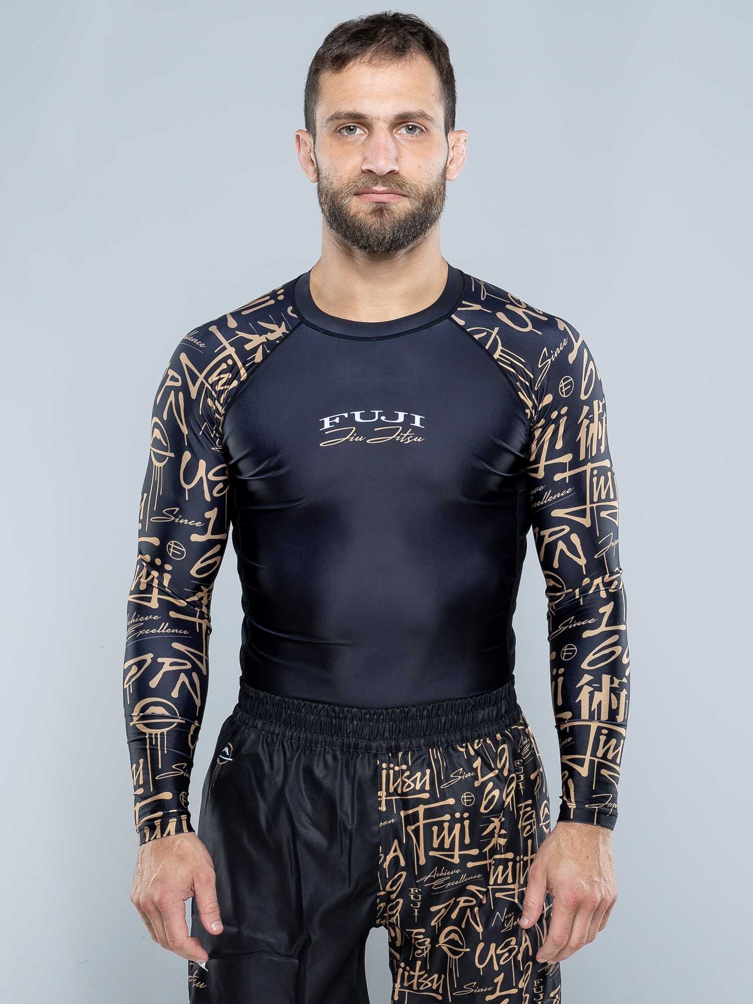 A man with short brown hair and a beard wears a black Shinobi Long Sleeve Rashguard against a plain gray background.