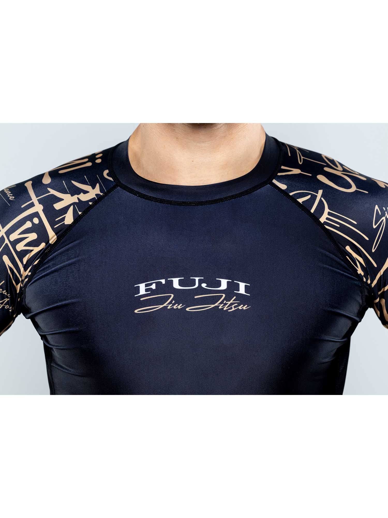 A person wearing the Shinobi Long Sleeve Rashguard Black, featuring gold accents and signature patterns on the sleeves. Only their upper torso and neck are visible.