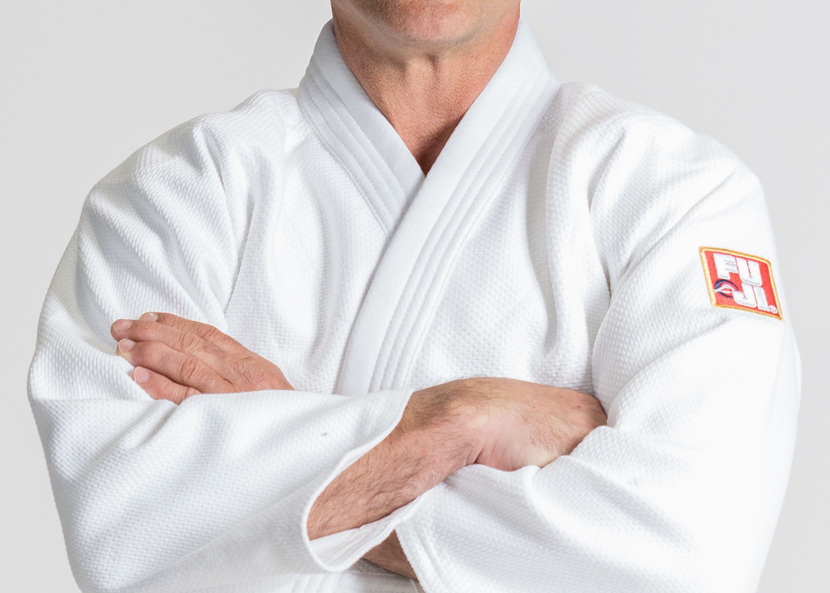 A person wearing a white martial arts gi with a FUJI patch on the sleeve stands with arms crossed, visible from shoulders to waist.