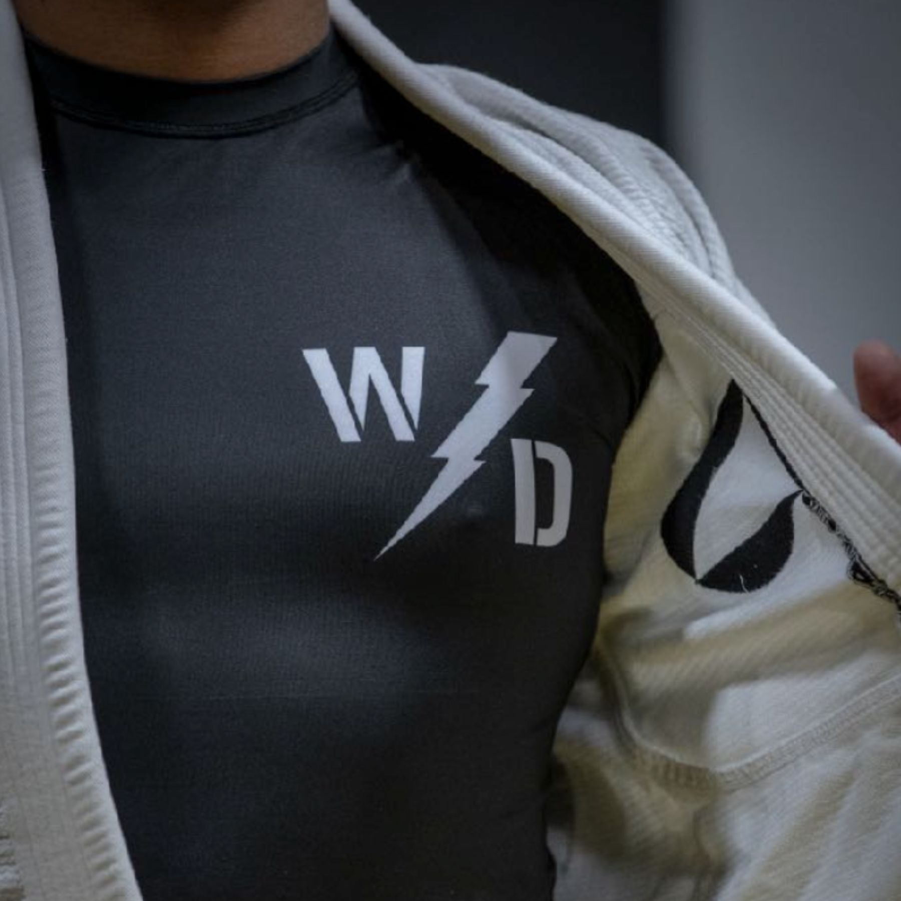 A person wearing a white martial arts gi opens it to reveal a black shirt with the letters W and D separated by a lightning bolt graphic on the chest.