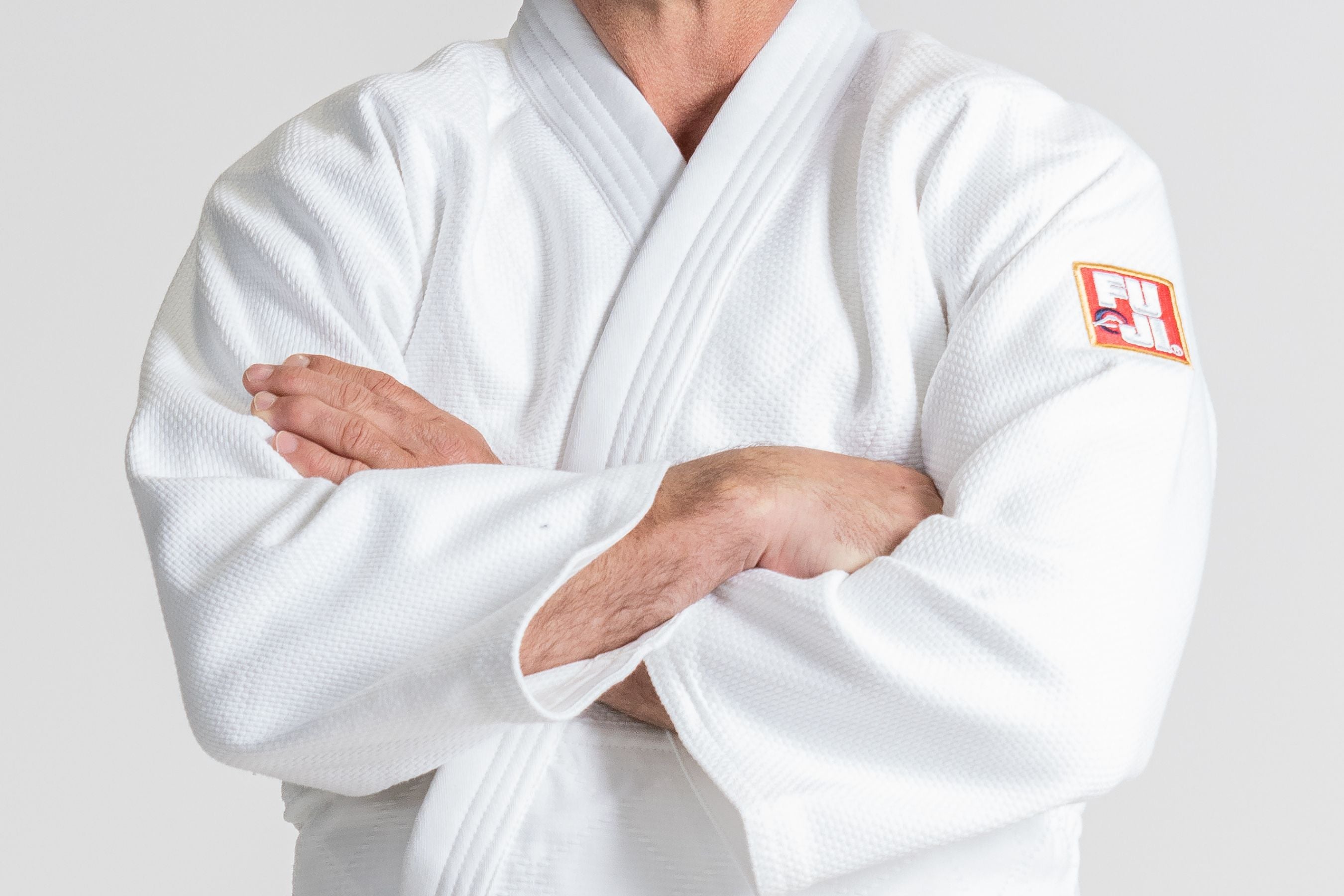 A person wearing a white martial arts gi with arms crossed. The uniform has a Fuji patch on the sleeve. The persons face is not visible.