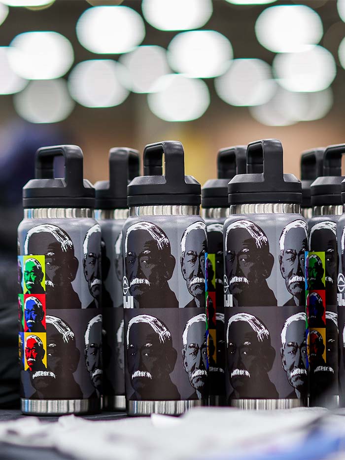 A group of Kano Tumbler 26oz stainless steel tumblers with black lids, each featuring a repeating portrait print of a man in pop-art color blocks.