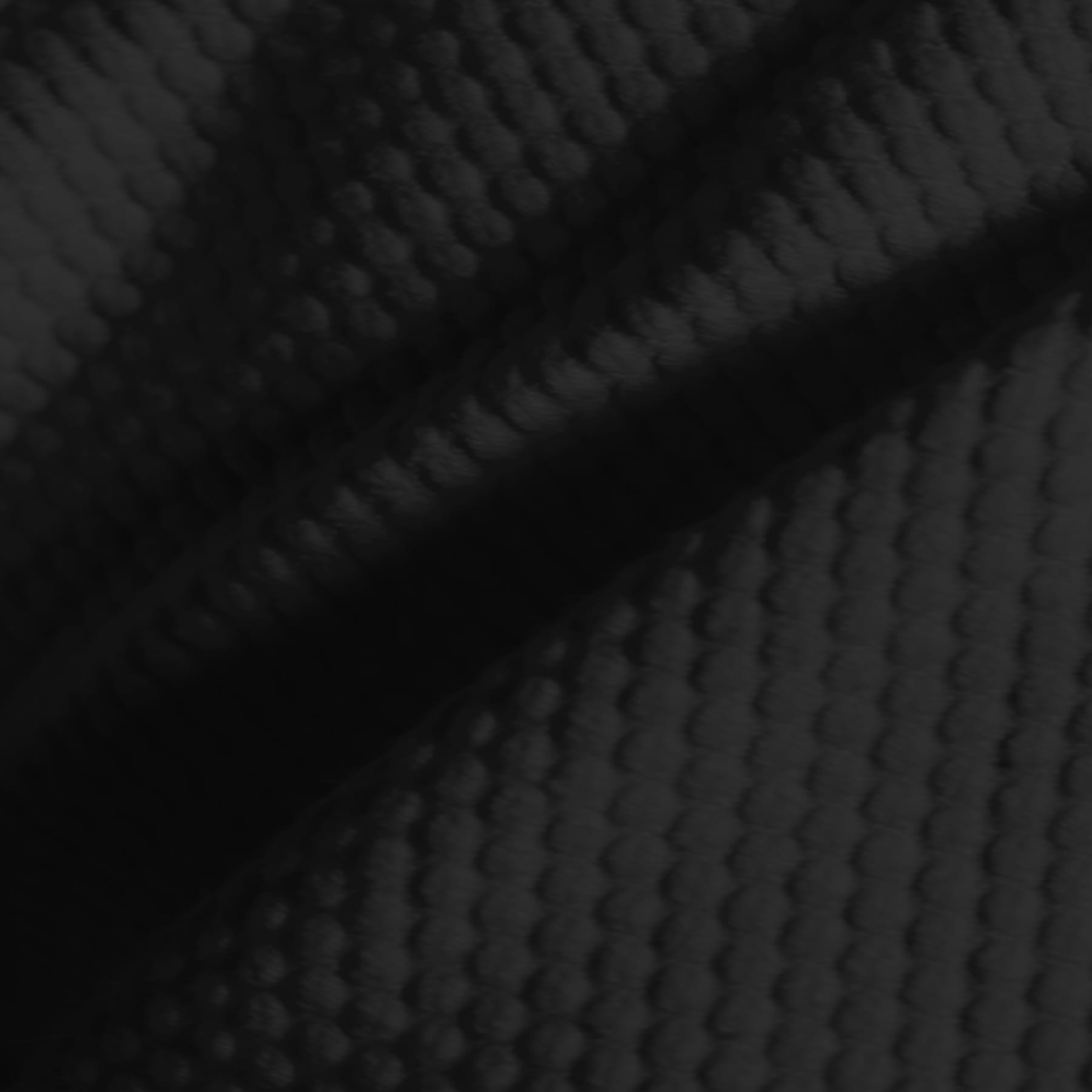 Close-up of dark, textured fabric with a waffle or honeycomb pattern, showing folds and shadows that emphasize the raised, grid-like surface.