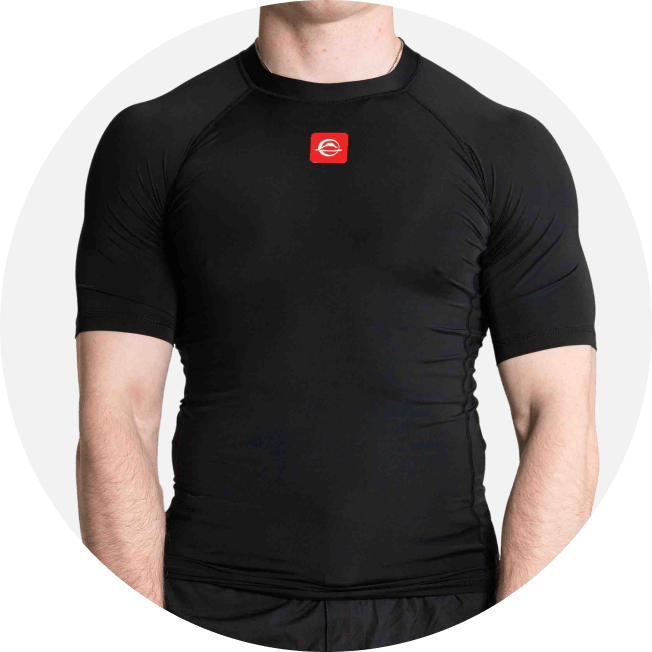 A person wearing a fitted black short-sleeve athletic rash guard with a small red logo on the chest, shown from the shoulders to the waist against a light gray background.