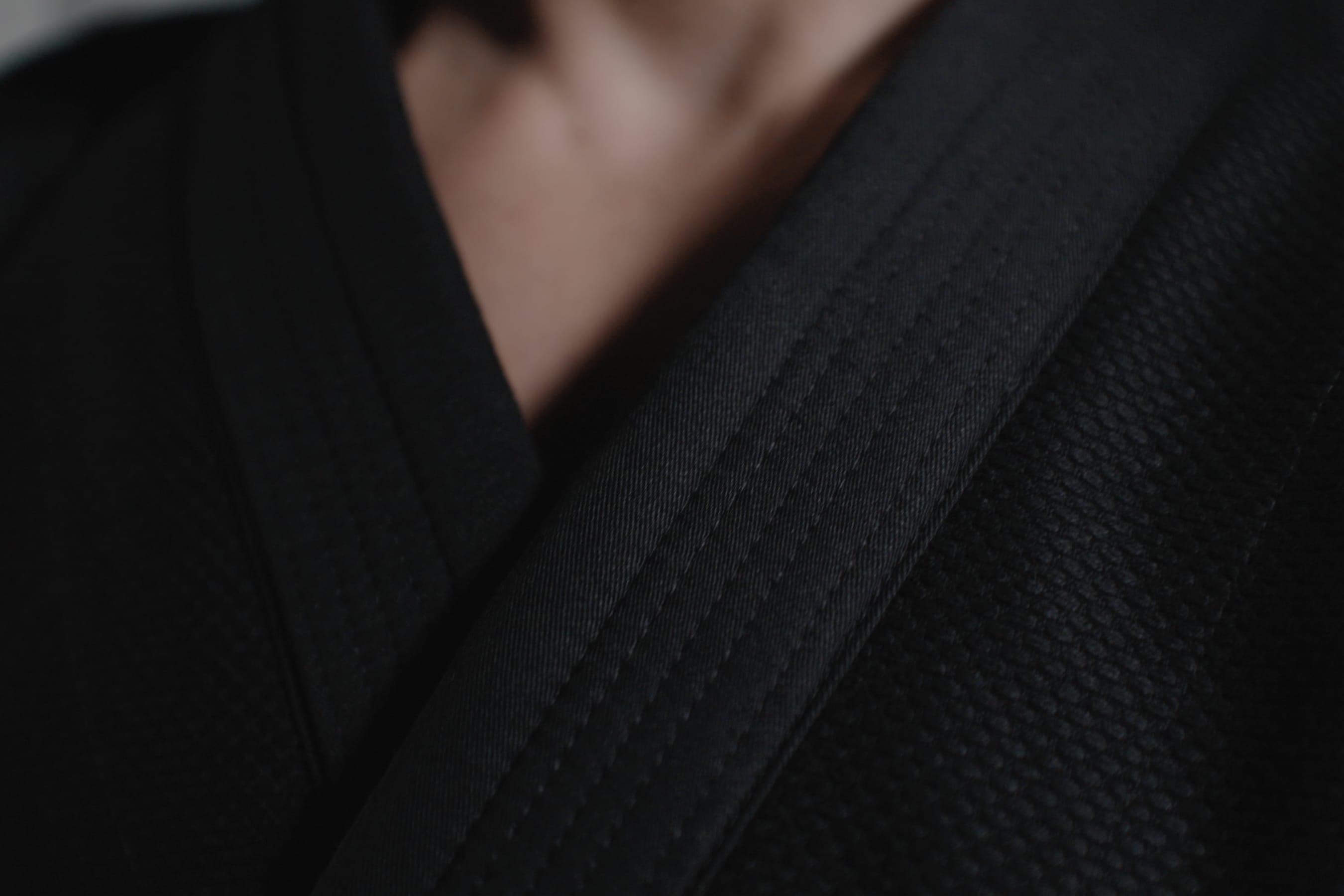 Close-up of a person wearing a black martial arts uniform, showing the textured fabric and the folded collar near the neck.