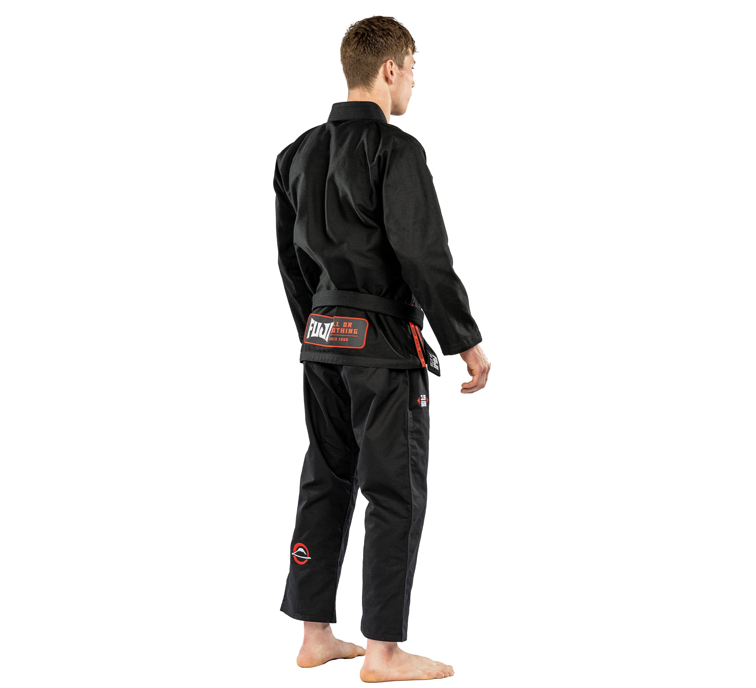 A person stands barefoot, facing away from the camera against a white background, wearing the Suparaito BJJ Gi Worldwide Edition Black with a belt.