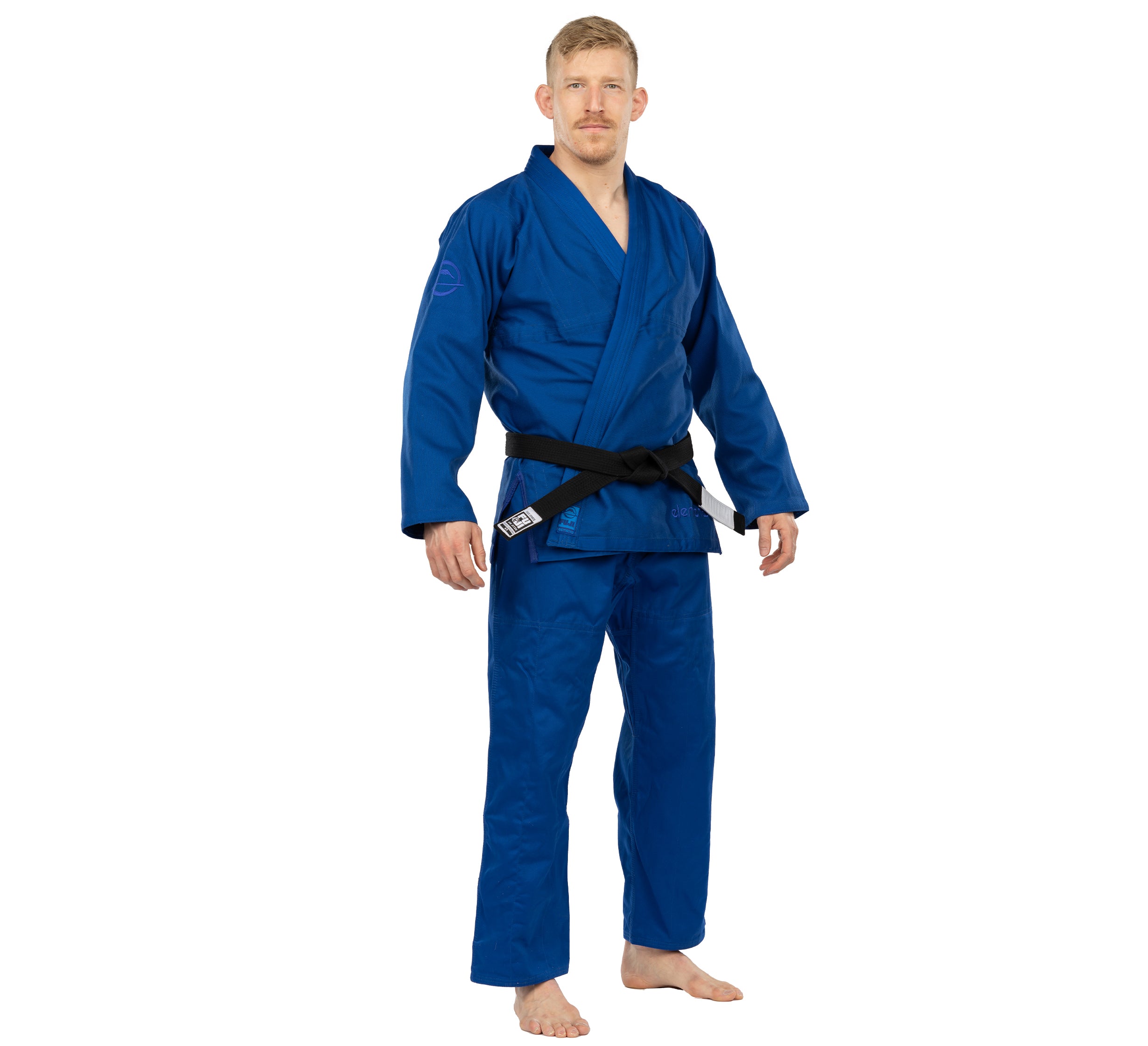 A man stands barefoot on a white background, wearing the Elemental BJJ Gi Blue with a black belt and looking forward with a neutral expression.