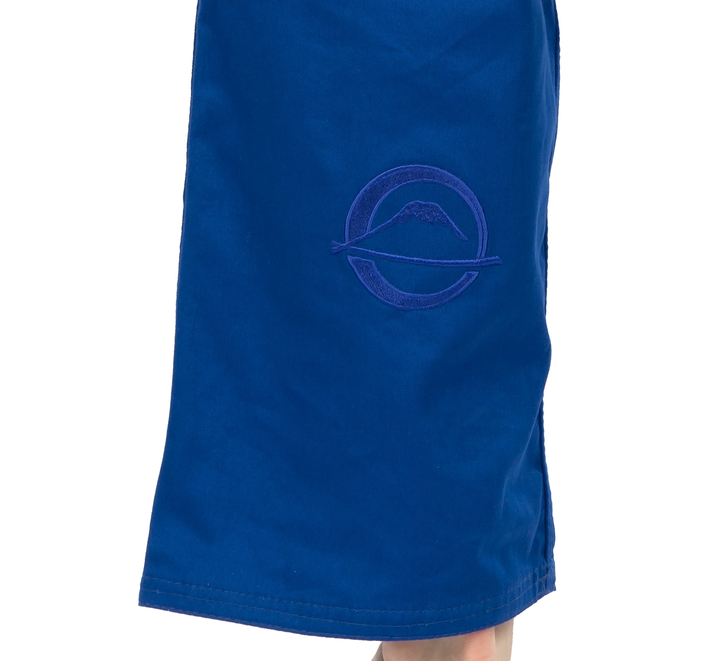 A close-up of someone wearing the Elemental BJJ Gi Blue, which features an embroidered circular mountain logo with a horizontal line on the side.