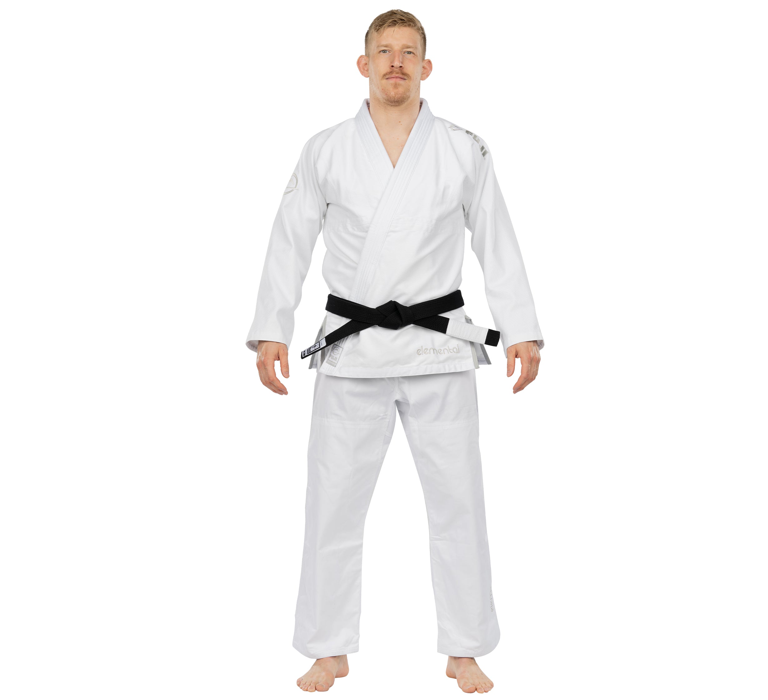 A man stands barefoot, facing forward, wearing the Elemental BJJ Gi White and a black belt, with his arms slightly out to the sides.