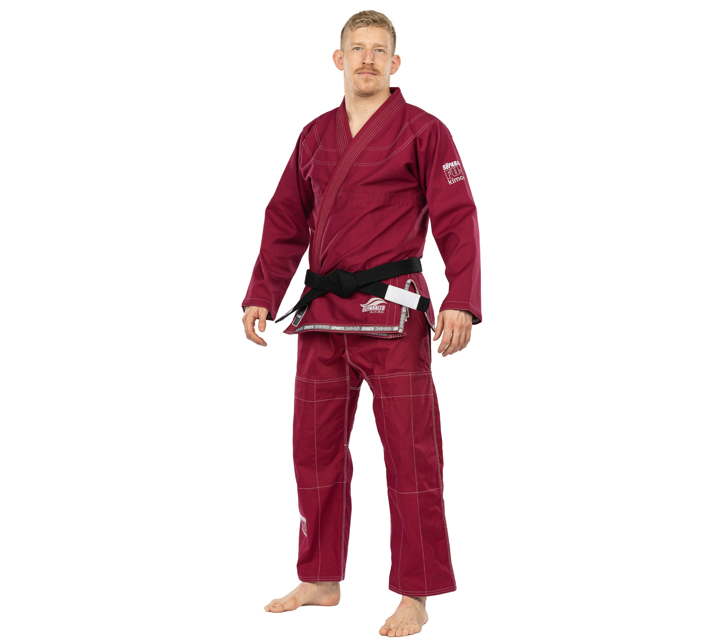 A man stands barefoot, facing forward against a plain white background, wearing the Suparaito BJJ Gi Burgundy with a black belt.