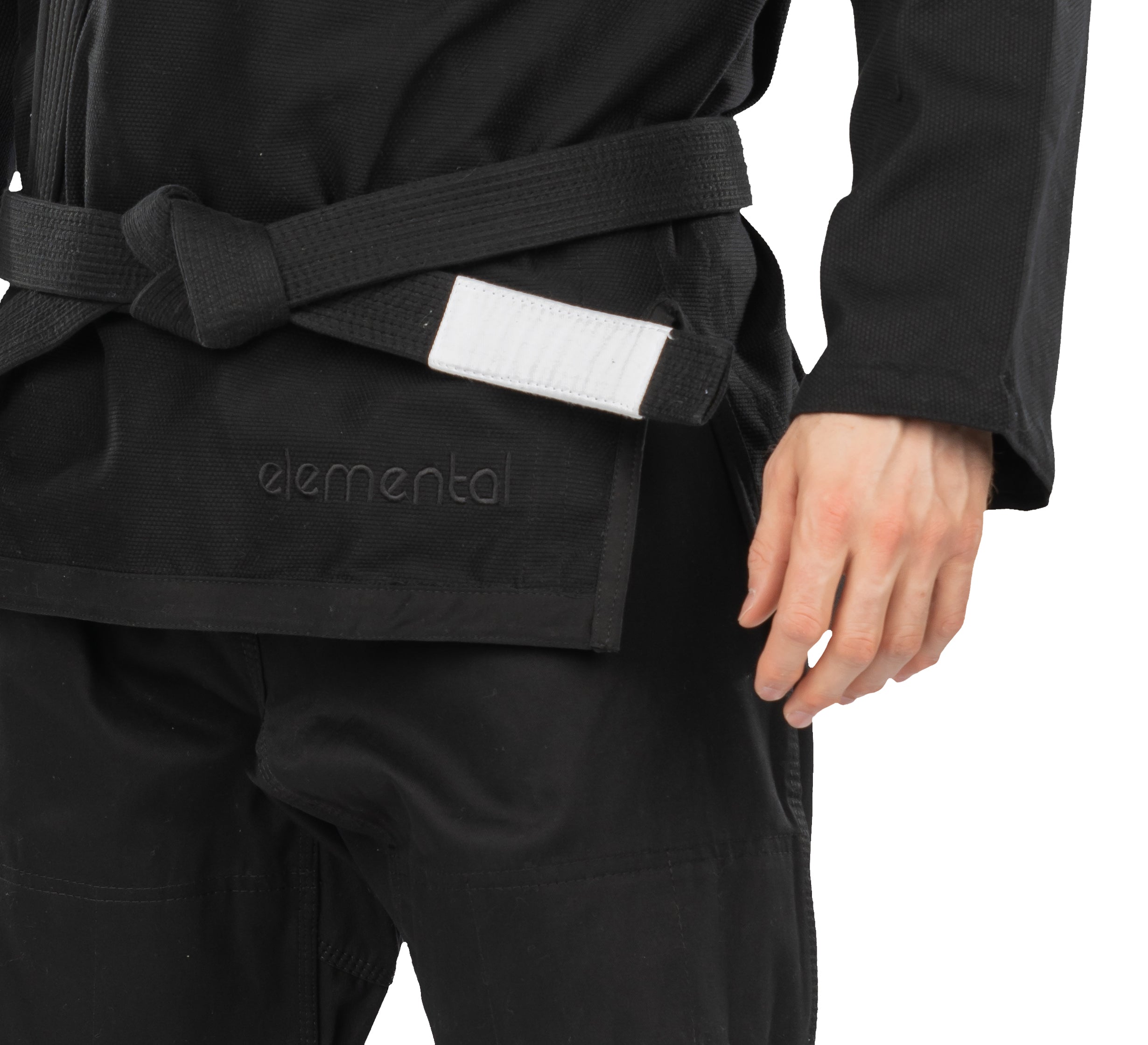 A person wears the Elemental BJJ Gi Black, featuring "elemental" embroidery and a black belt with a white patch, shown waist down with one arm visible.