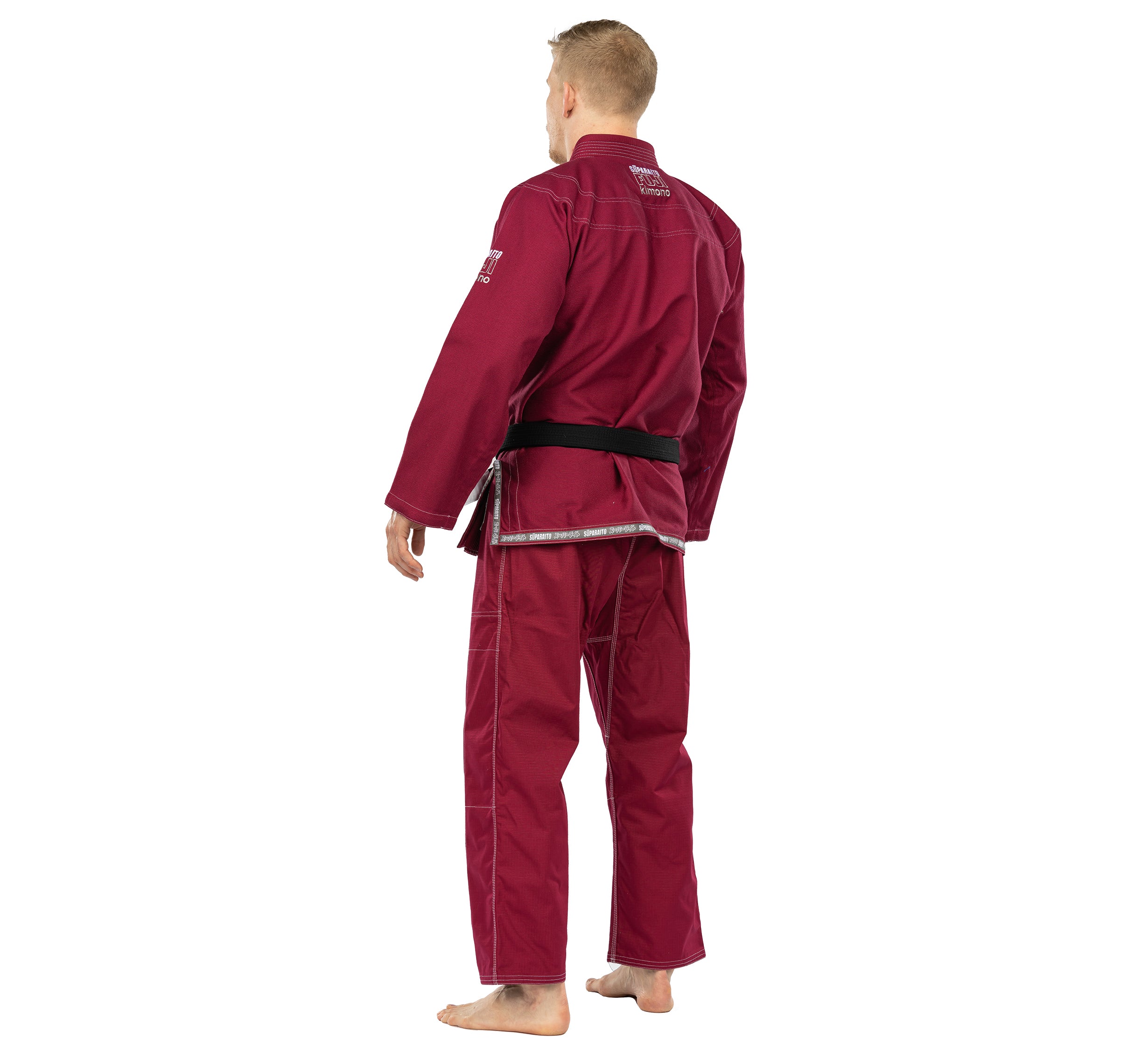 A man stands barefoot facing away from the camera, wearing the Suparaito BJJ Gi in burgundy with a black belt, set against a white background.