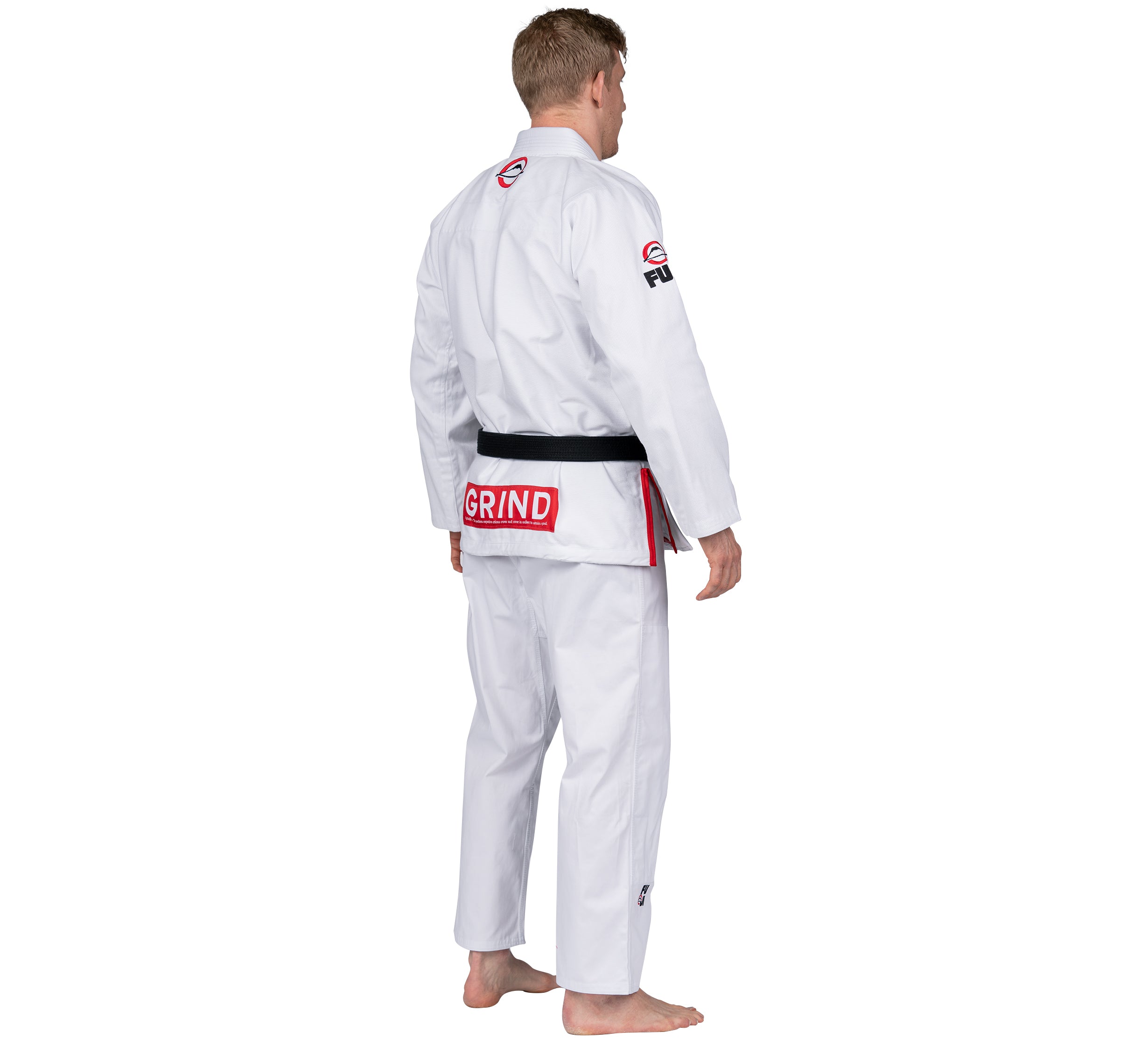 A barefoot person, seen from behind, wears the Elemental BJJ Gi Grind White—a white martial arts gi with a black belt and red and black patches, including "GRIND" on the back waistband.
