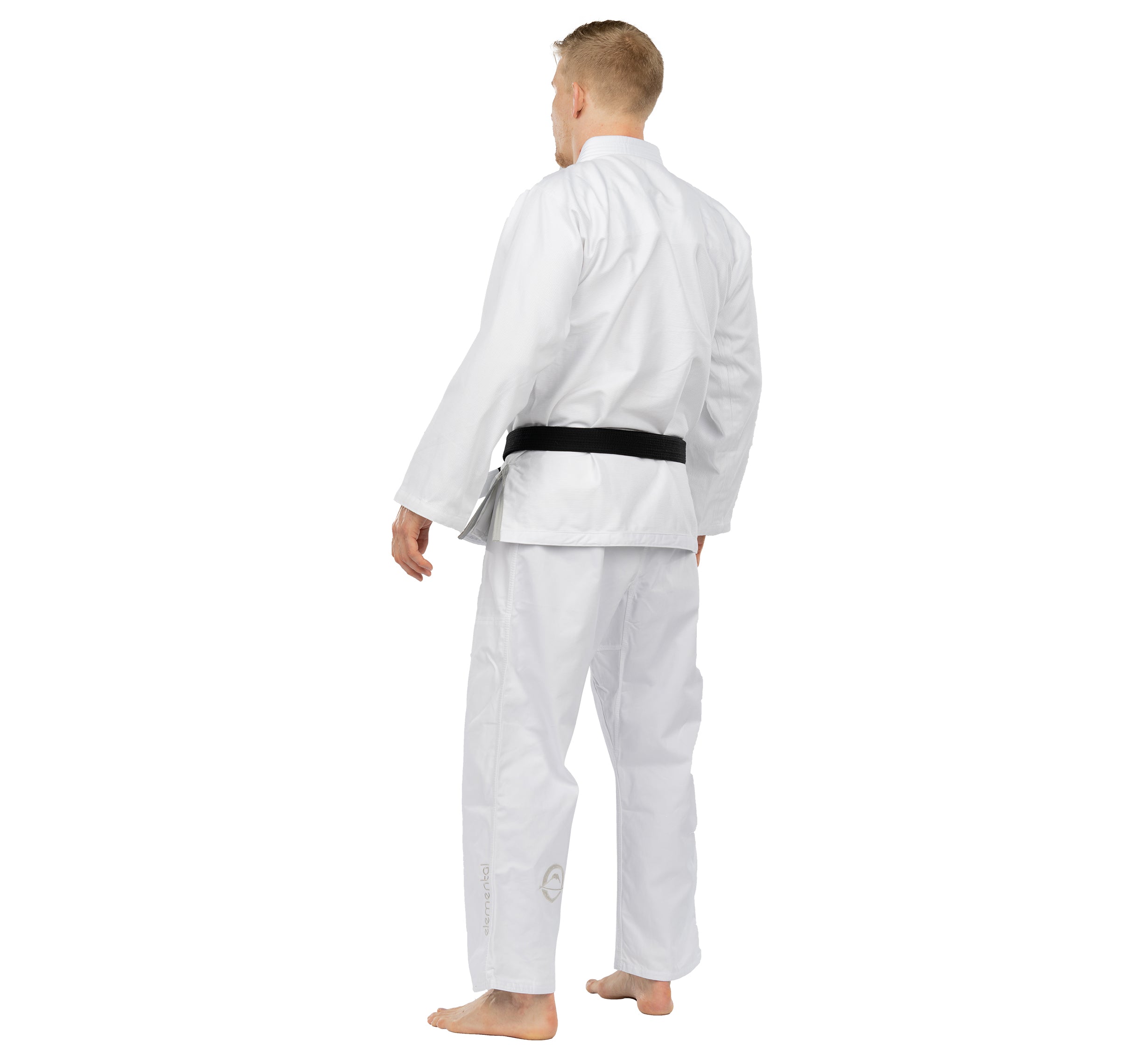 A barefoot man wears the Elemental BJJ Gi White and a black belt, standing with his back turned and head slightly to the side, set against a white background.