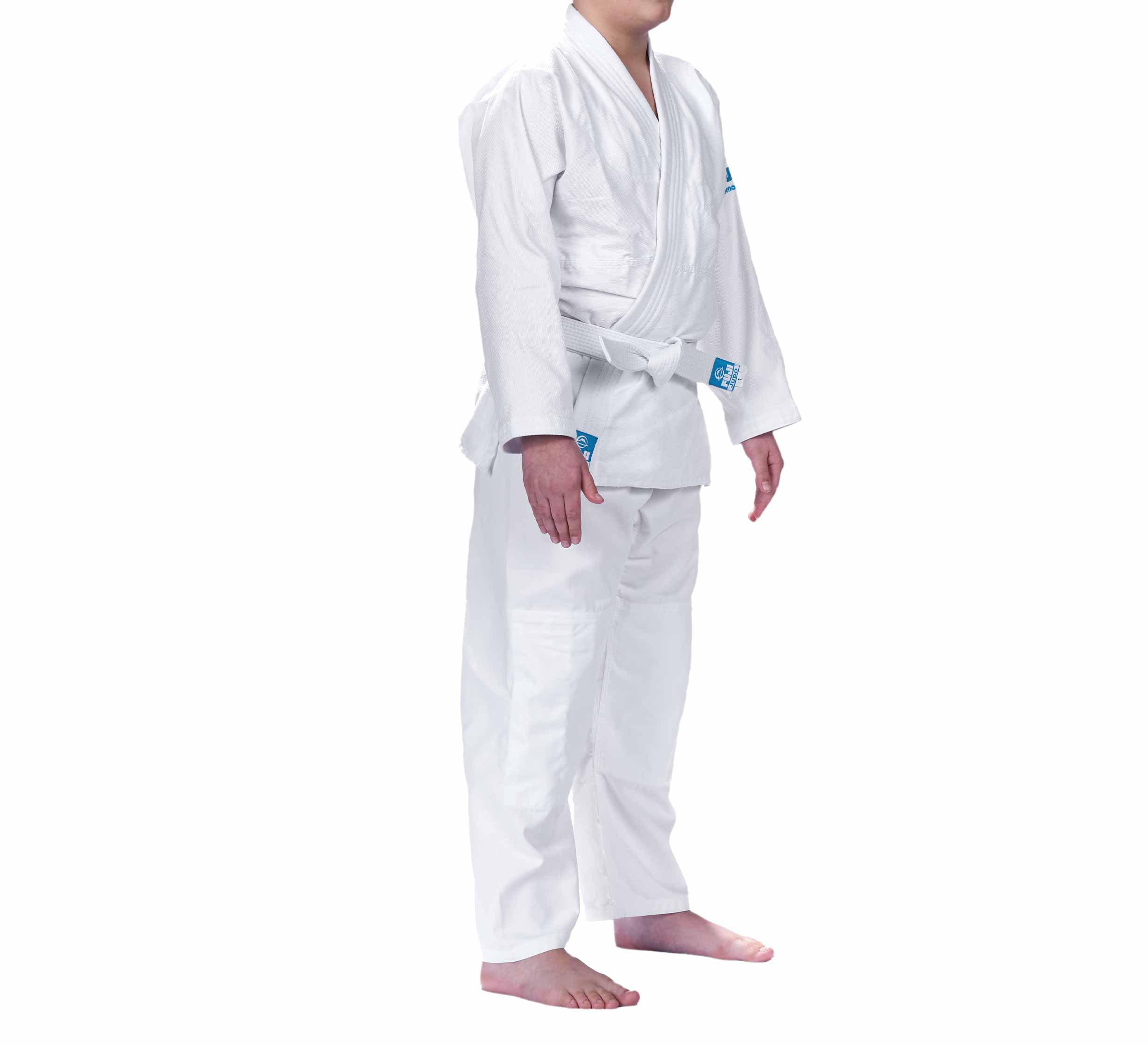 A child models the Starter Kids Judo Gi—a white martial arts uniform with a white belt—standing barefoot against a plain white background, face not shown.