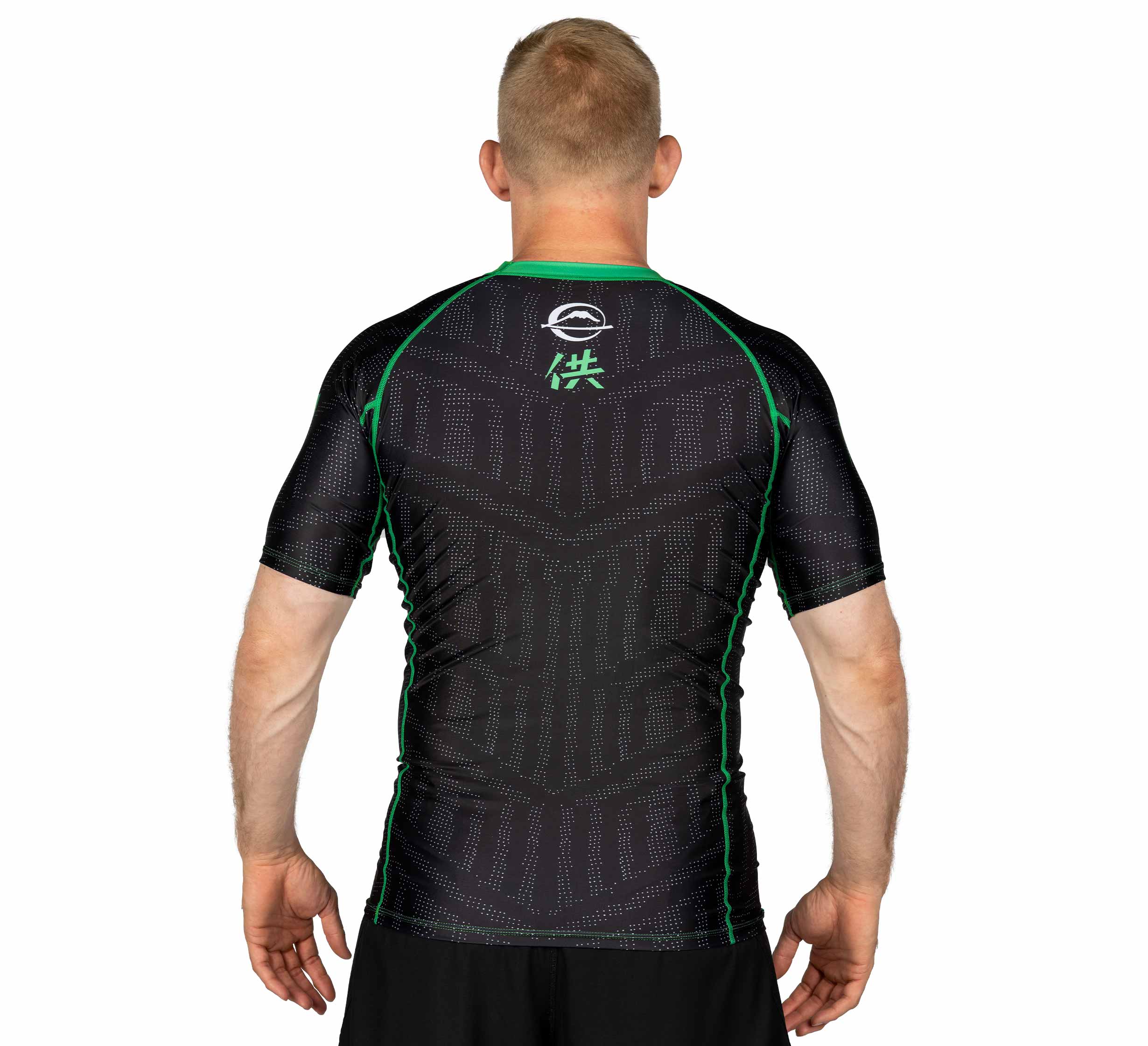 A man with short blond hair, seen from behind, wears the Team FUJI Short Sleeve Rashguard Green—a fitted black athletic shirt featuring green trim, subtle geometric patterns, and a white logo with Asian characters on the upper back.