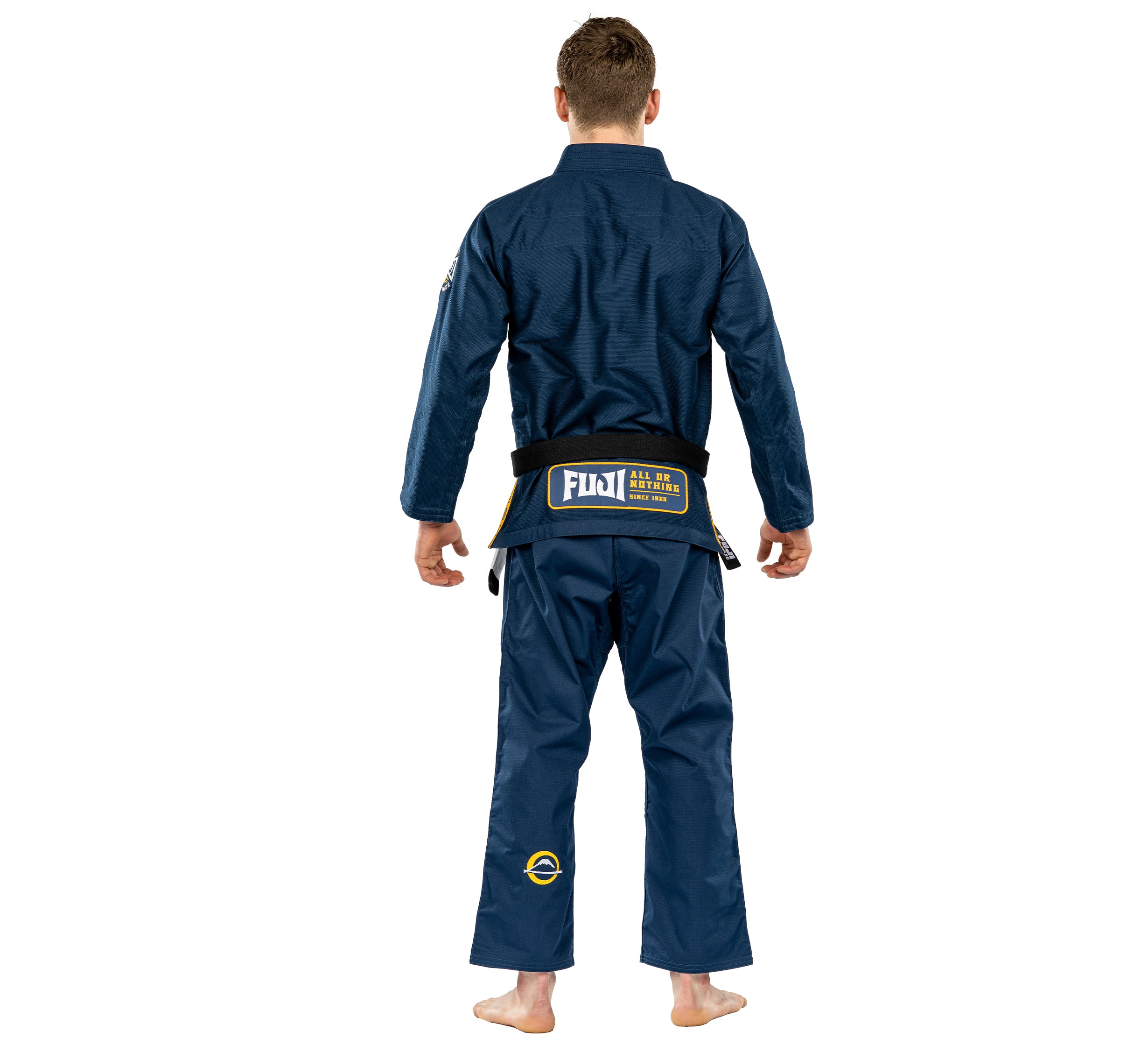 A person stands barefoot with their back to the camera, arms relaxed, wearing the Suparaito BJJ Gi Worldwide Edition Navy and a black belt.