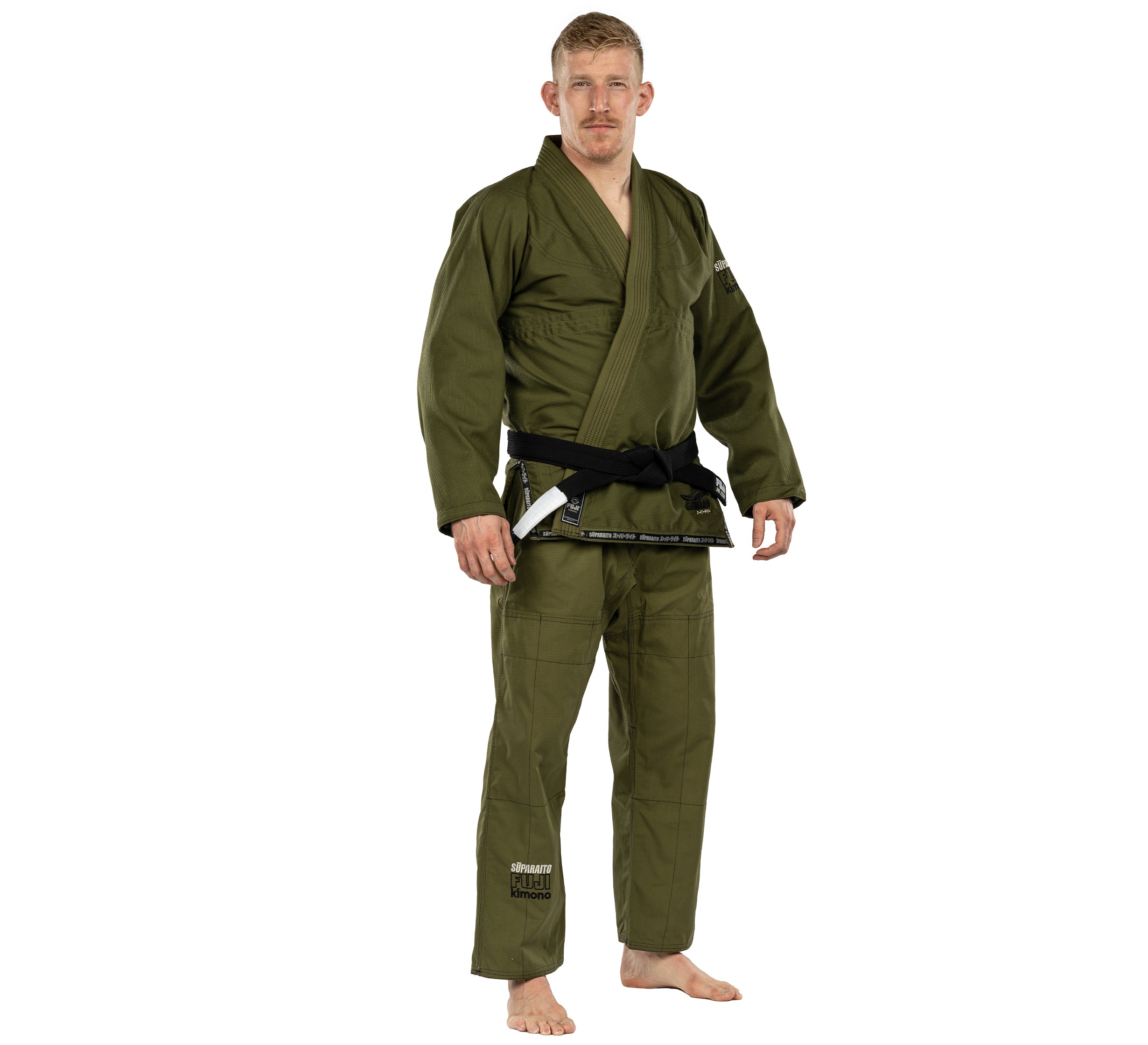 A man with short blond hair and a mustache stands barefoot in an olive green Suparaito BJJ Gi with a black belt, posing seriously against a plain white background.