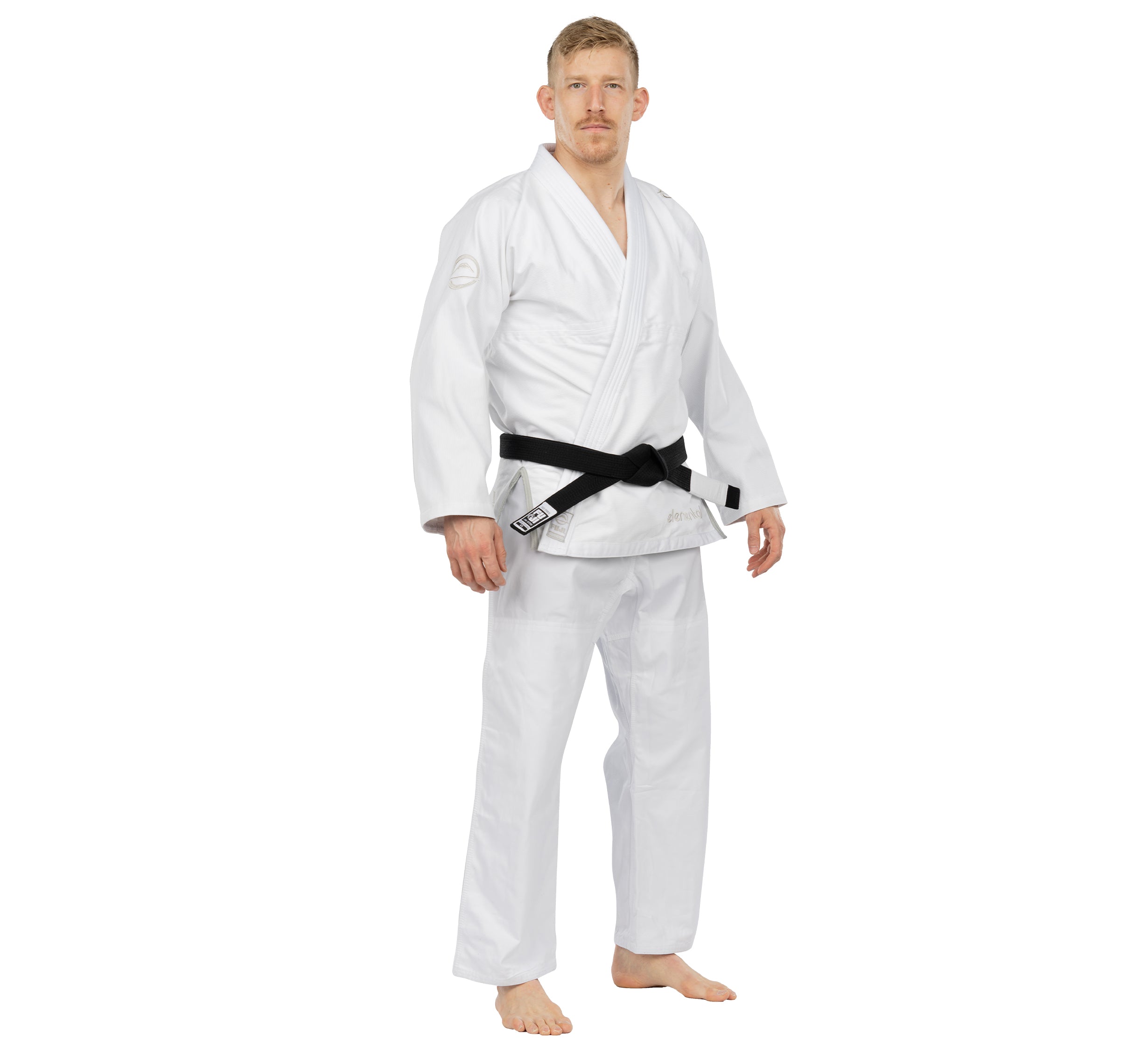 A man stands barefoot in the Elemental BJJ Gi White with a black belt, looking ahead with a neutral expression against a plain white background.