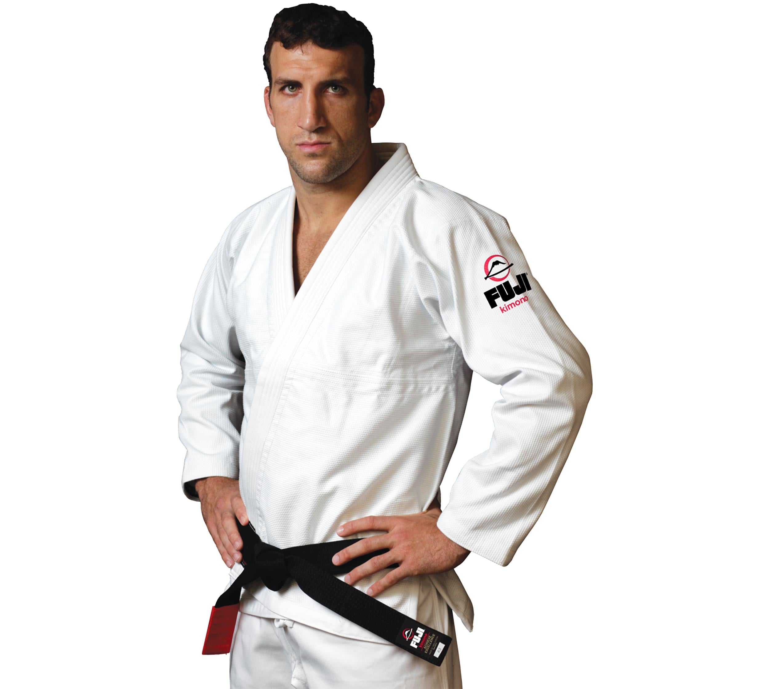 A man stands with hands on hips, looking forward, wearing the All Around BJJ Gi—a white martial arts gi with a black belt and a Fuji logo on the sleeve. The background is white.